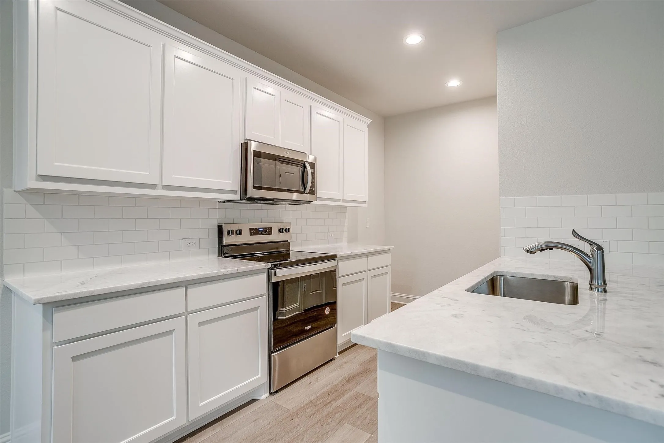White cabinetry, subway tile backsplash, stainless steel appliances, undermount sink, and wood-finish flooring