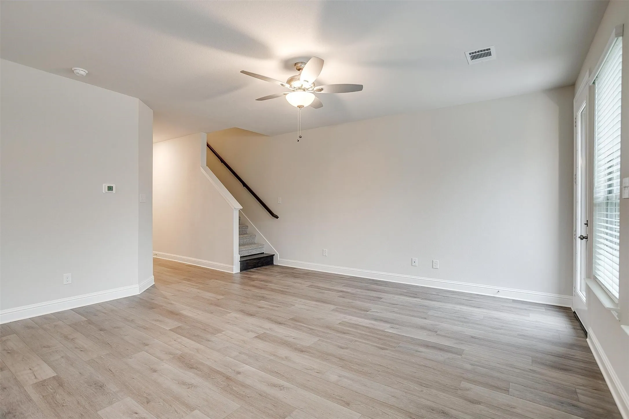 Wood-finish flooring, ceiling fan with integrated lighting, white walls, white trim, and a staircase with a dark wood handrail