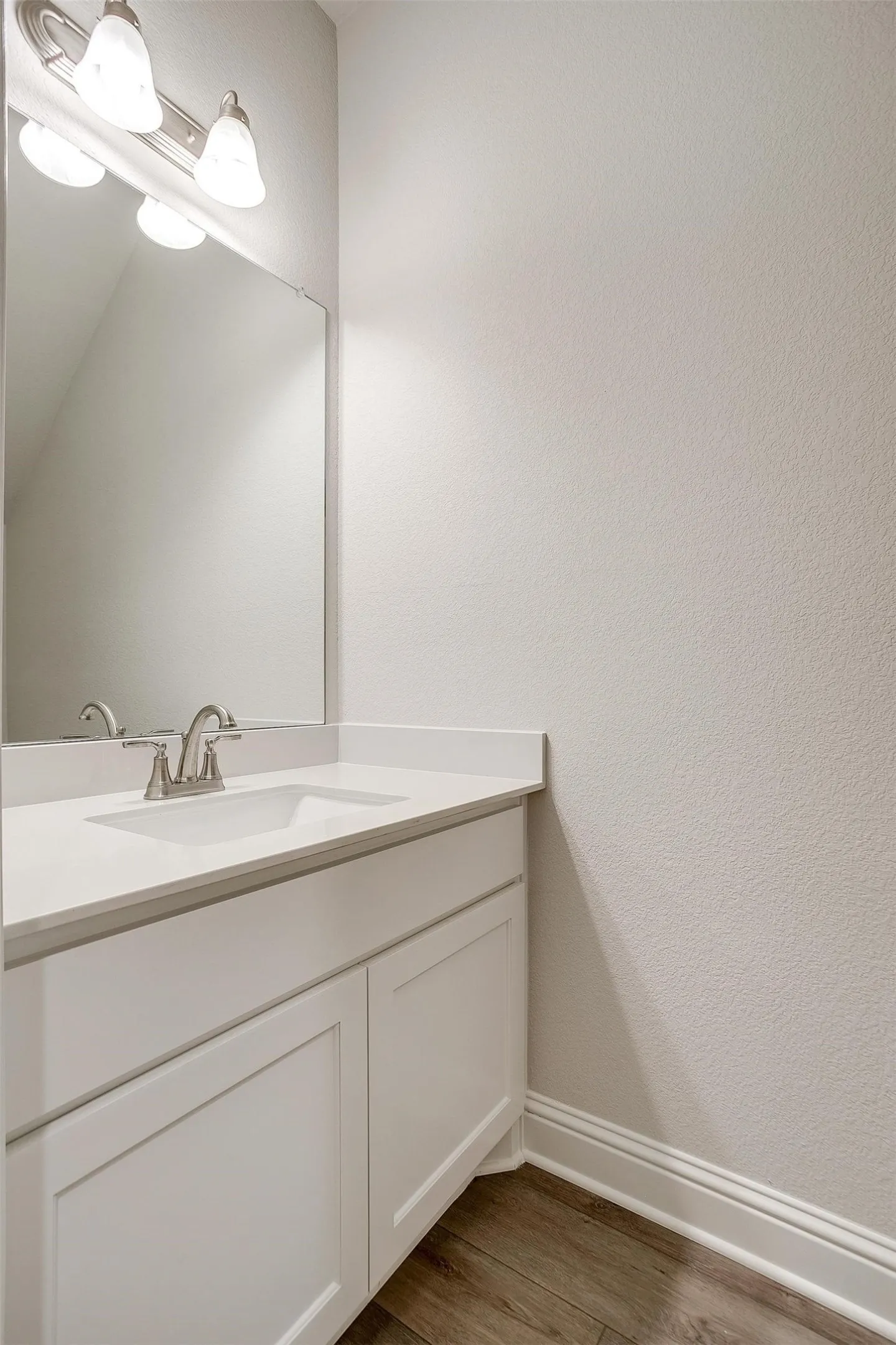 White vanity with Shaker-style cabinet doors, brushed nickel faucet, integrated sink, and wood-finish flooring