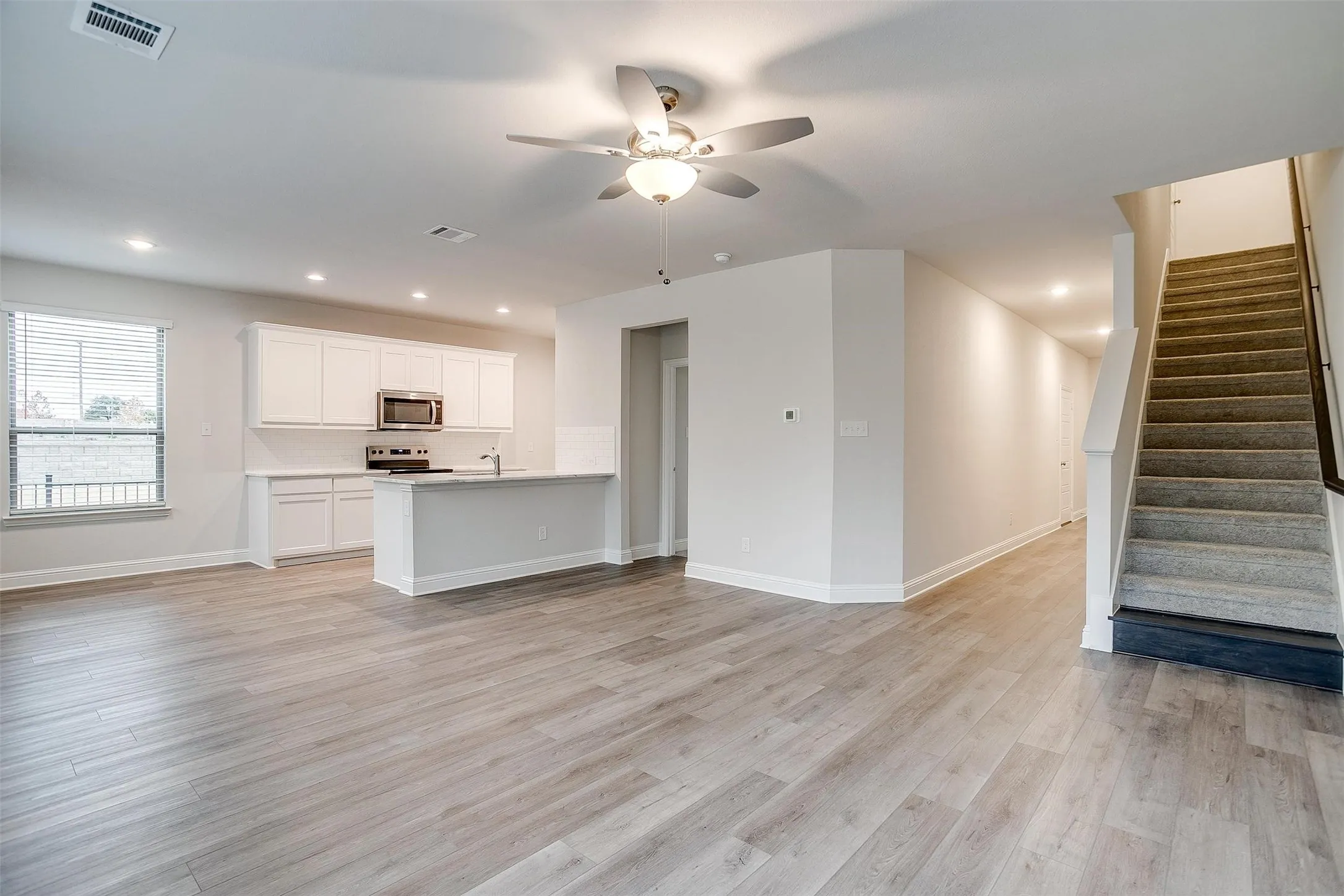 Open-concept living area featuring wood-finish flooring, recessed lighting, a ceiling fan, and white kitchen cabinetry with stainless steel appliances
