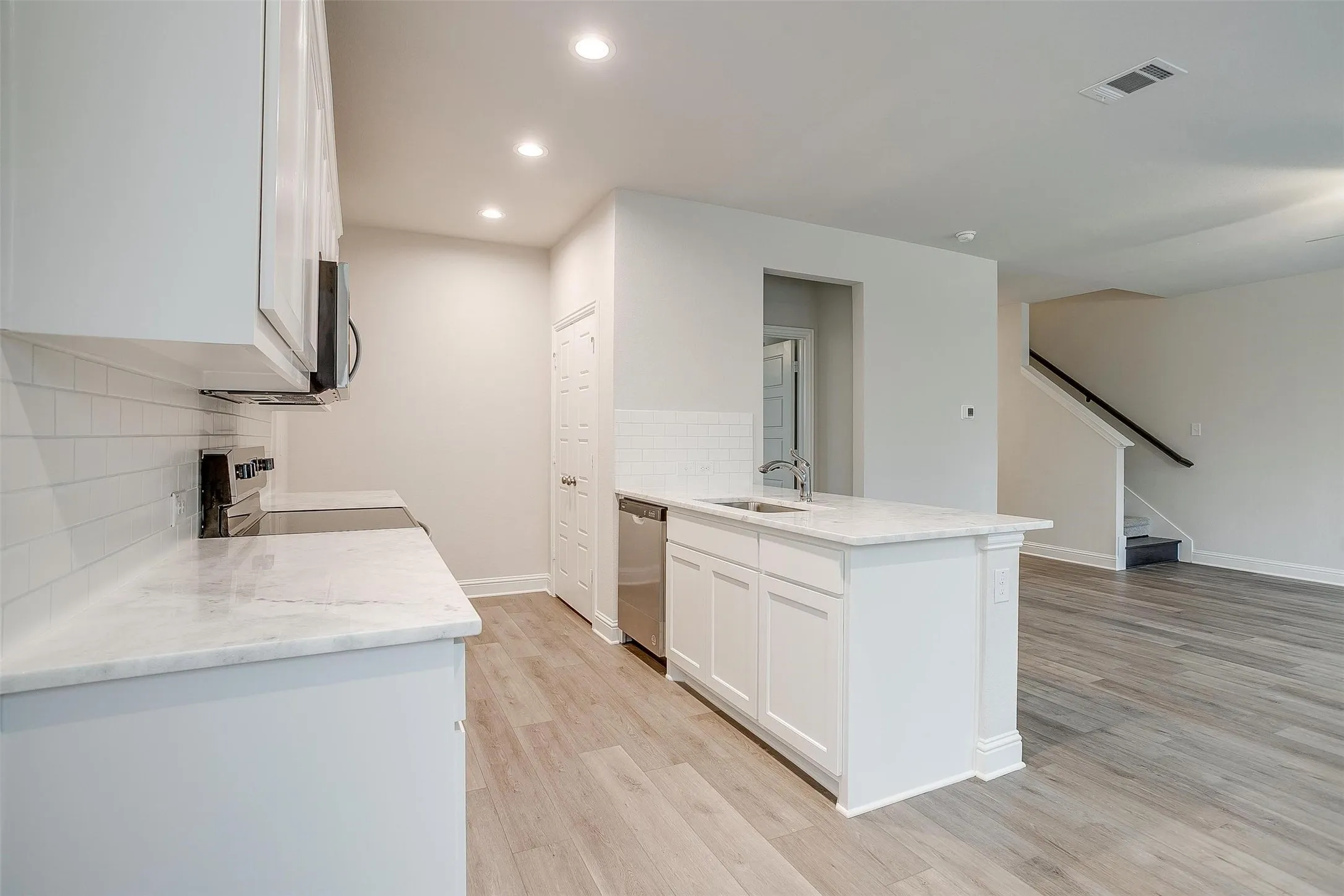 Modern kitchen with stainless steel appliances, white cabinetry, a kitchen island with sink, and light wood-finish flooring