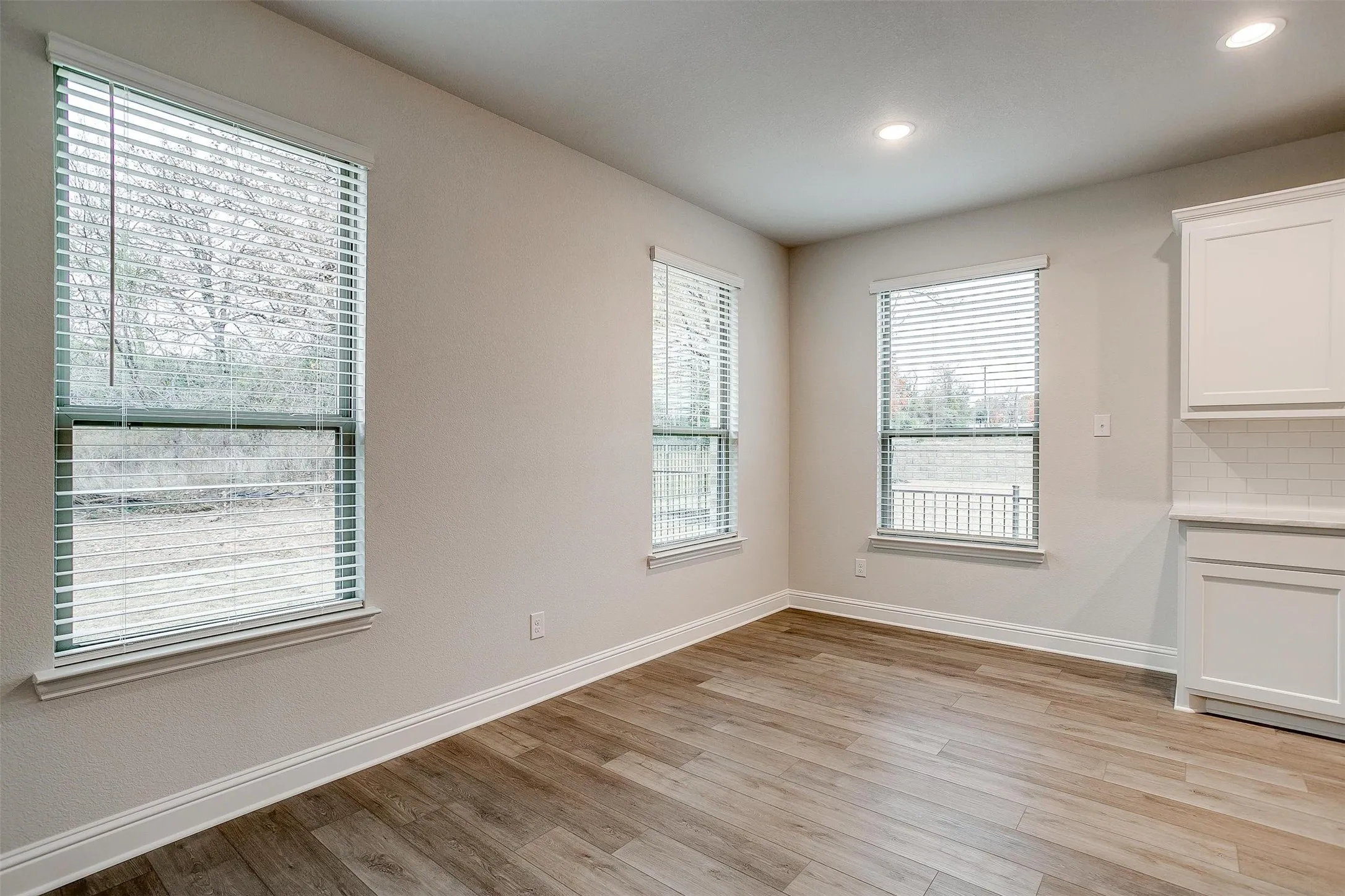 Wood-finish flooring, recessed lighting, multiple windows with blinds, white cabinetry, and white subway tile backsplash
