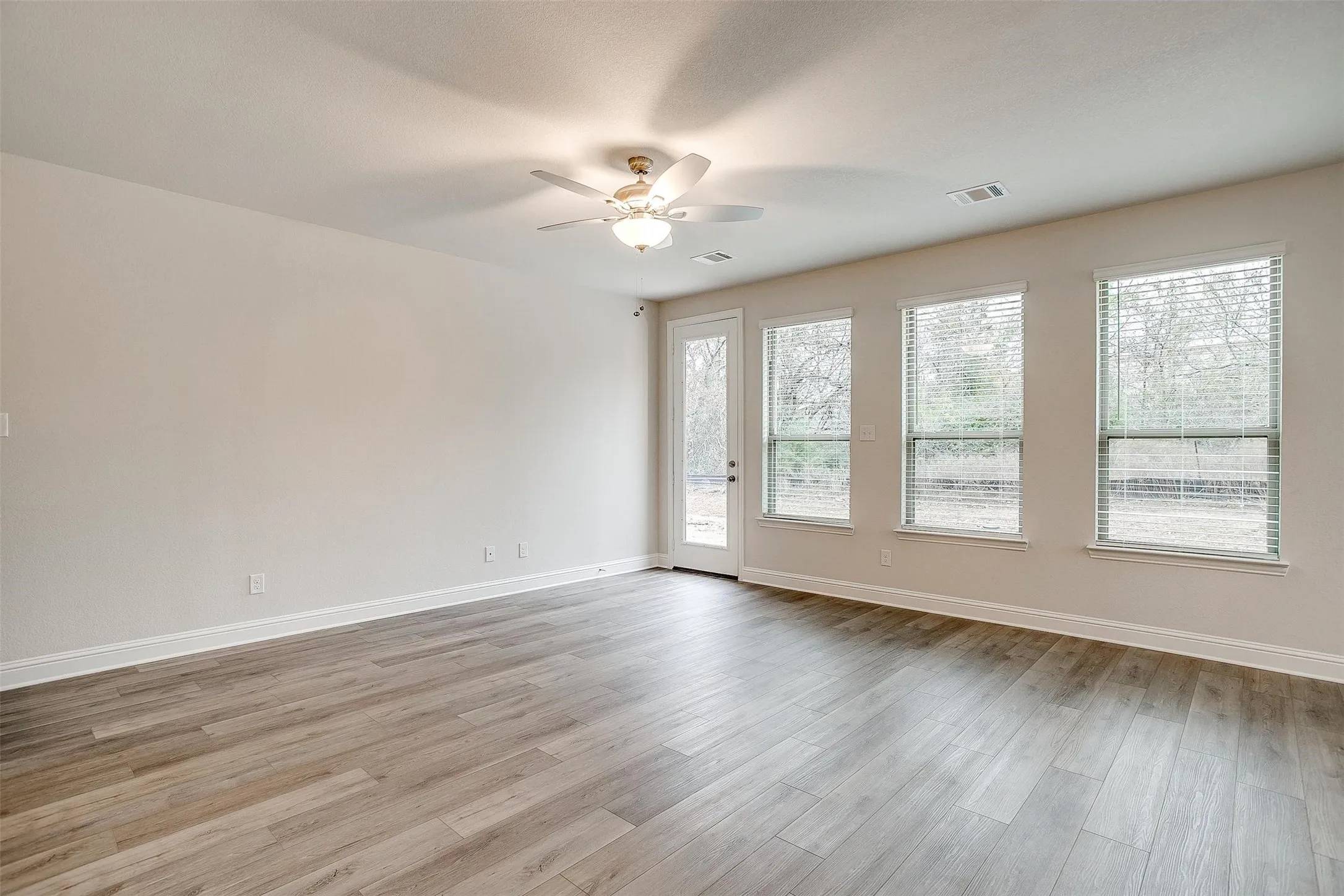 Wood-finish flooring, multiple windows with blinds, a ceiling fan, and a single glass-paneled door