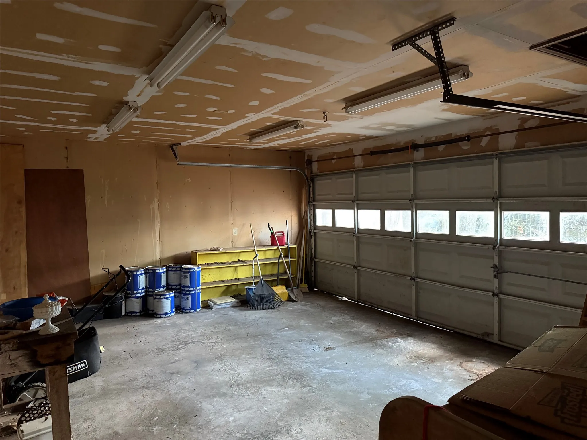 Attached garage with a concrete floor, equipped with fluorescent lighting fixtures, and featuring a panel garage door with integrated windows
