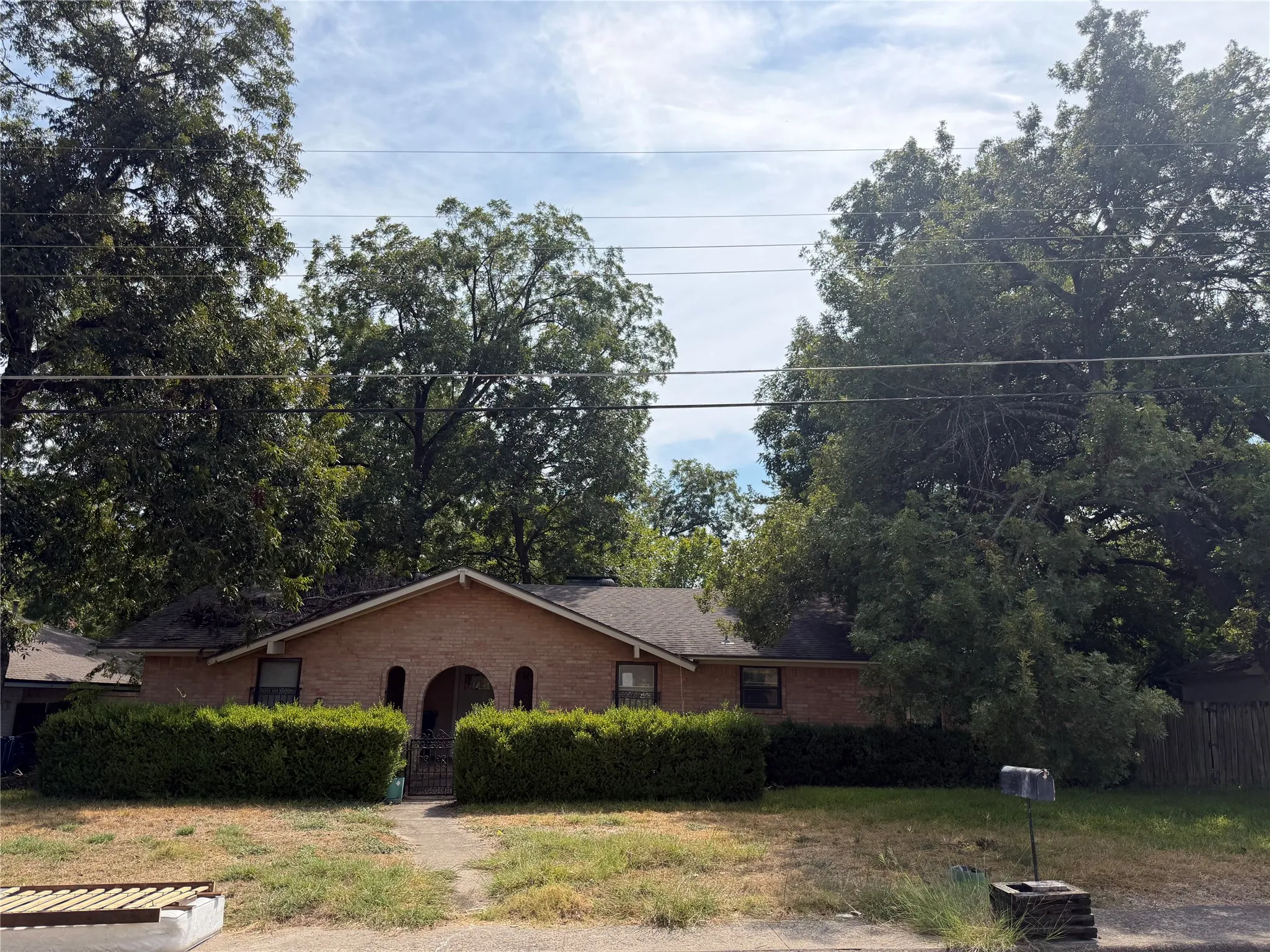 Brick exterior with an arched entryway, manicured front hedges, and mature trees