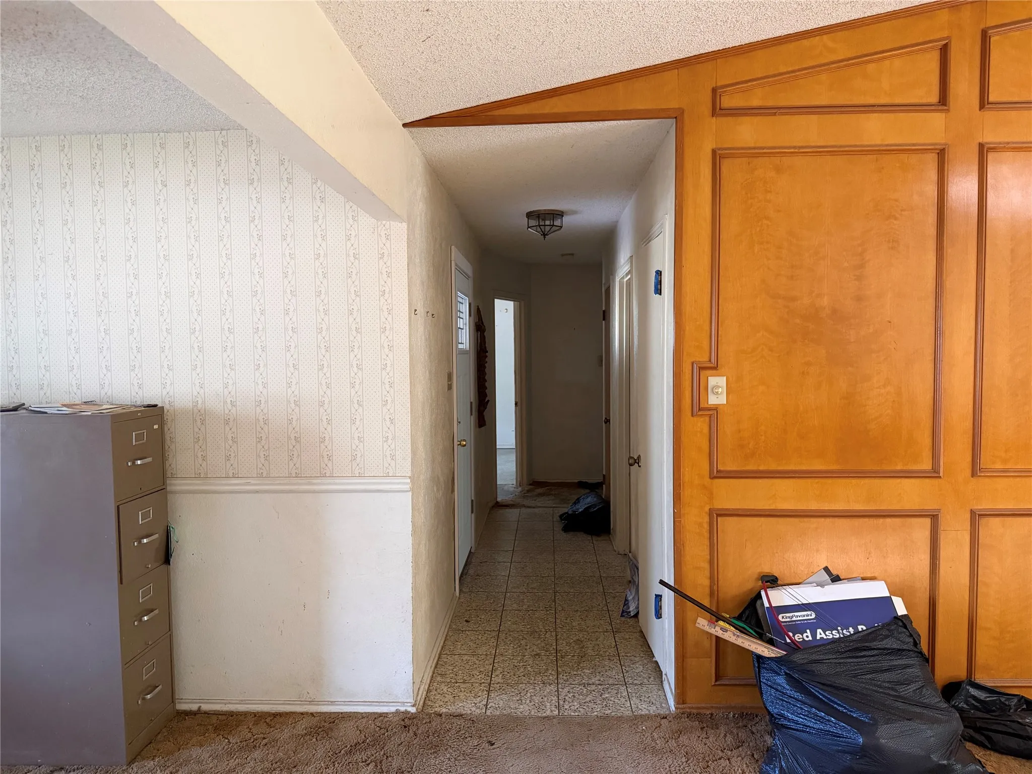 Wood-paneled accent wall, textured wallpaper, wainscoting, tiled flooring, and popcorn ceiling