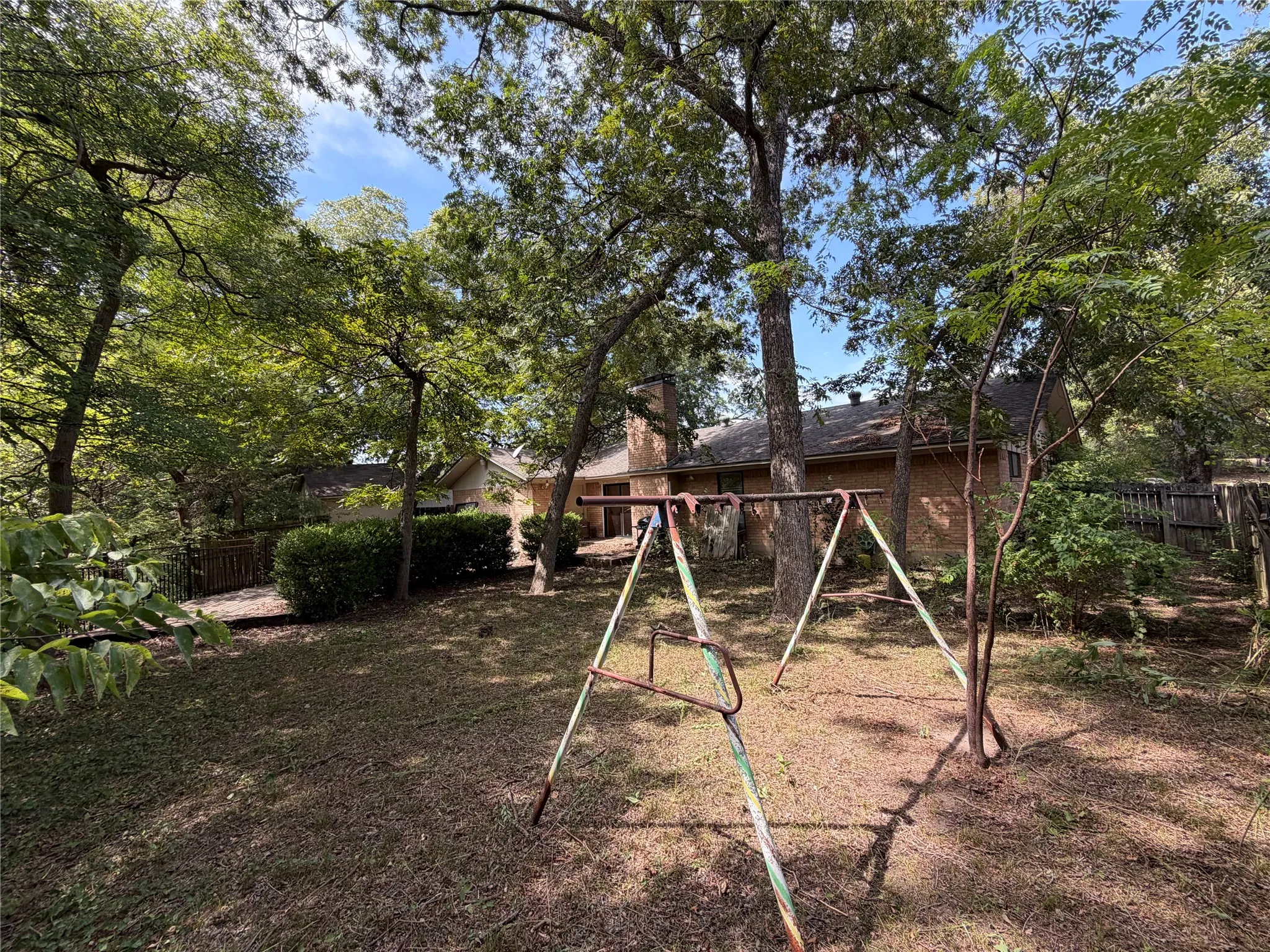 Expansive rear yard featuring mature trees, a brick exterior, and a sloped terrain