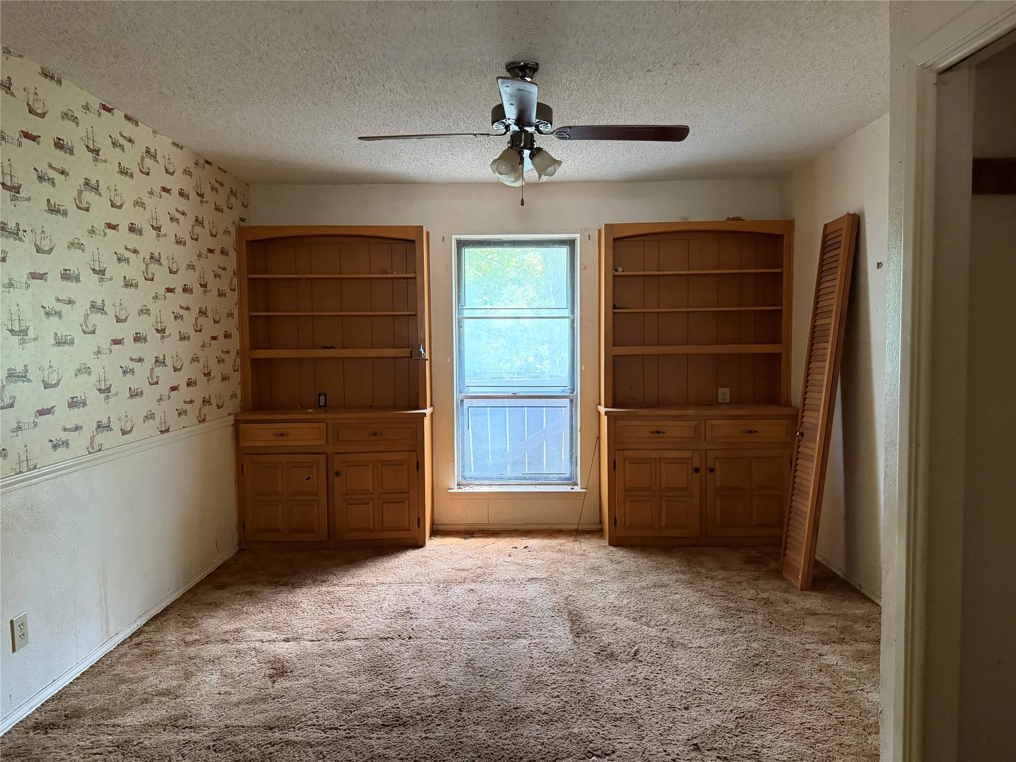 Built-in wood shelving units, overhead ceiling fan with light fixture, carpeted flooring, and a single window