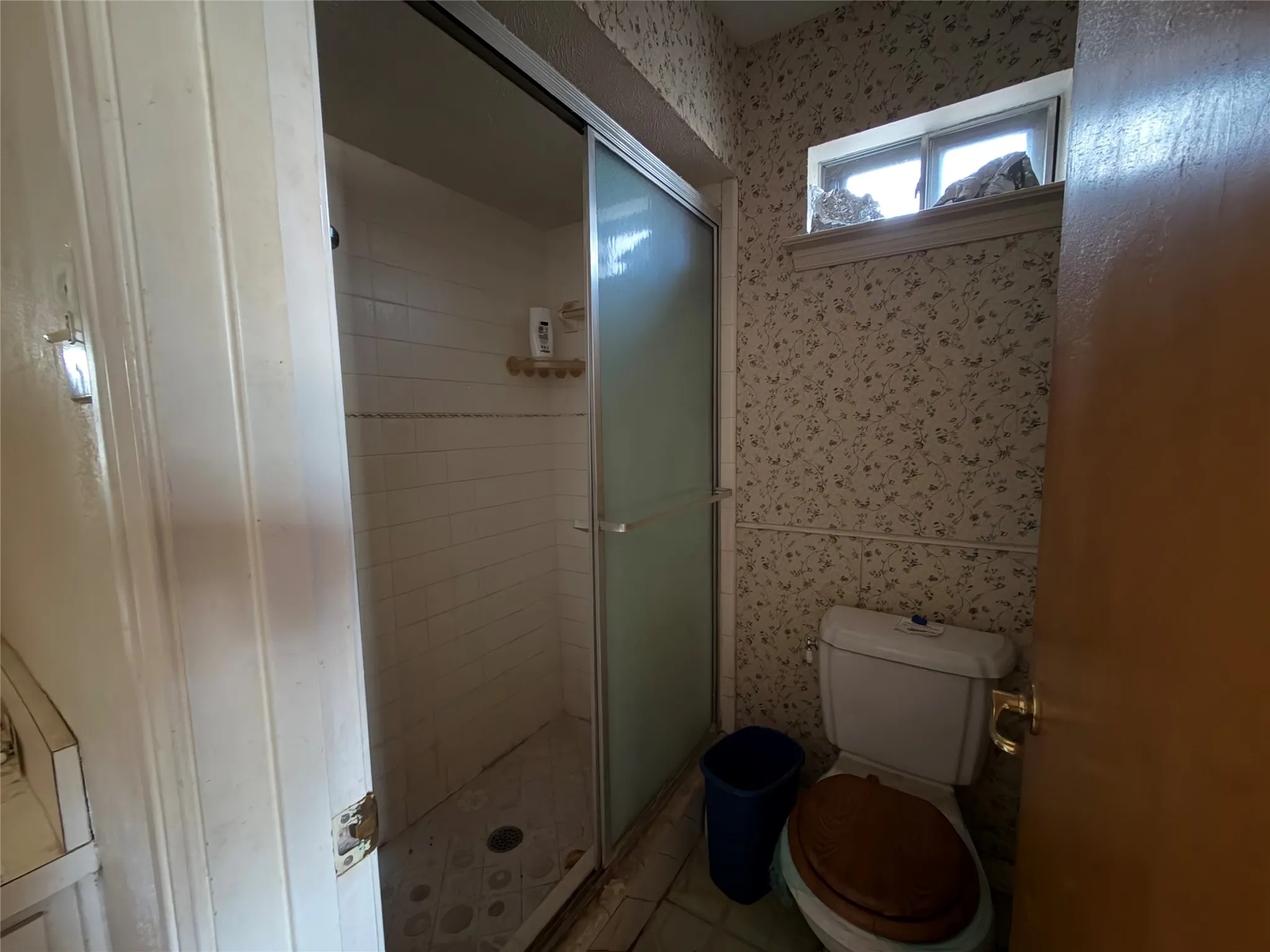 Shower with sliding glass doors, white tiled walls, and patterned wallpaper