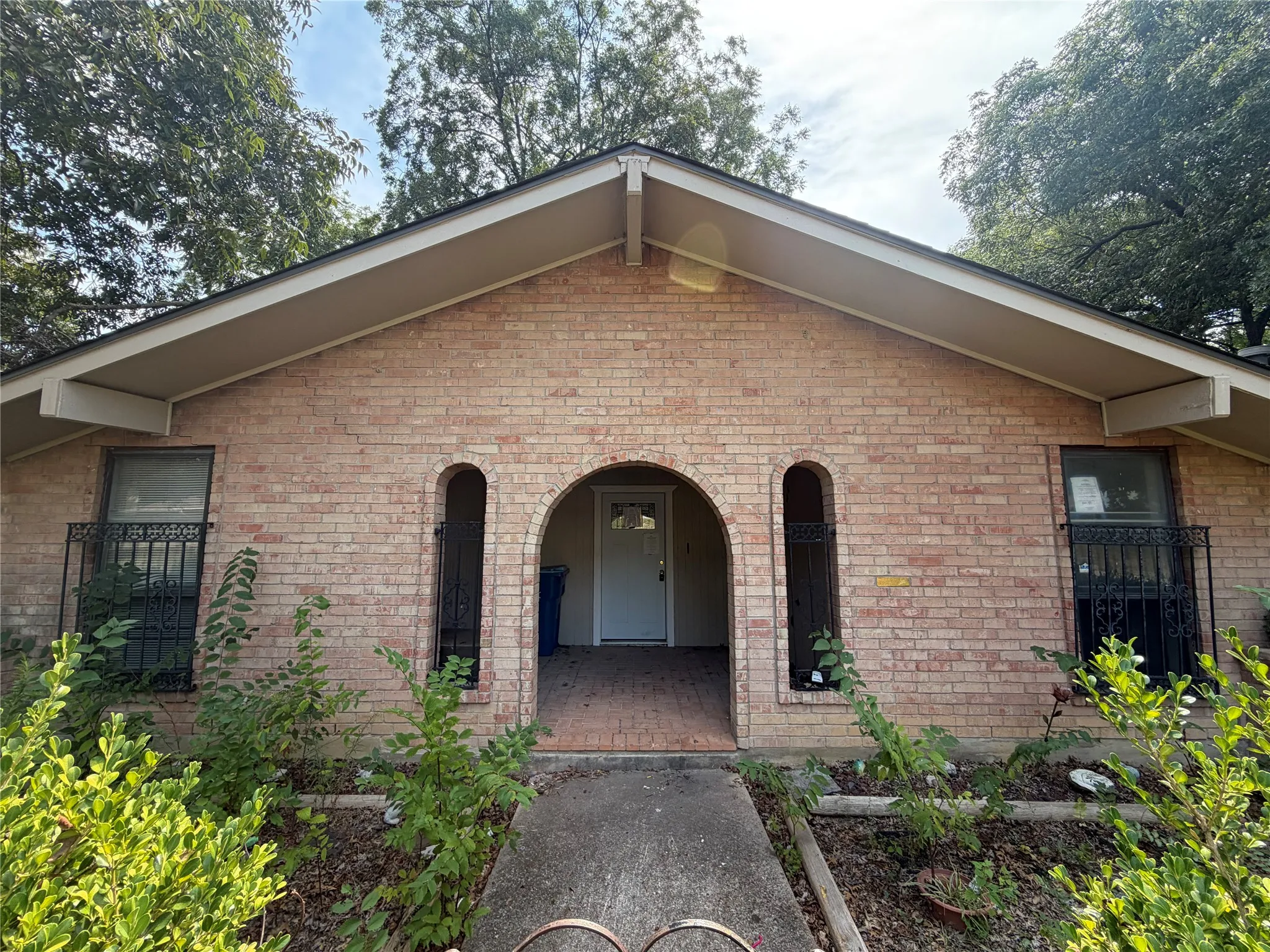 Brick facade with arched entryways, gabled roofline, and decorative window security bars
