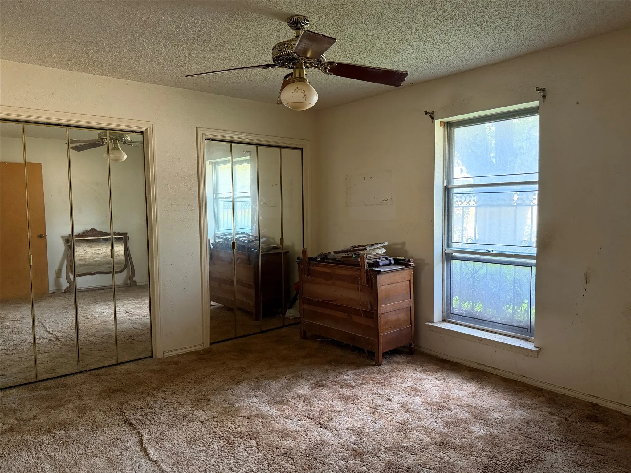 Spacious primary bedroom featuring ceiling fan with integrated lighting, mirrored sliding closet doors, large window with natural light, and carpeted flooring throughout