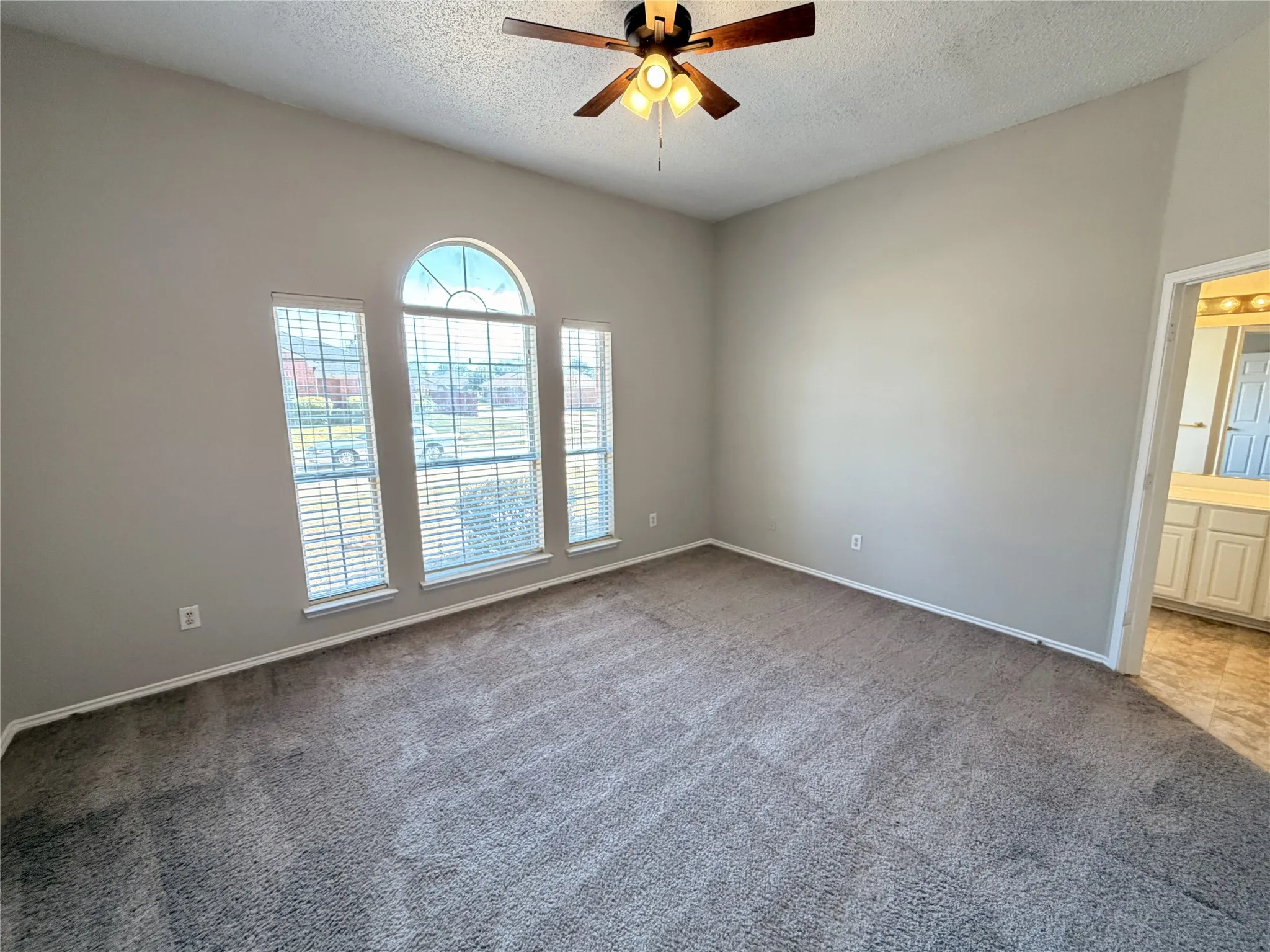 Room featuring textured carpeting, a trio of windows including an arched transom, a ceiling fan with integrated lighting, and neutral wall paint