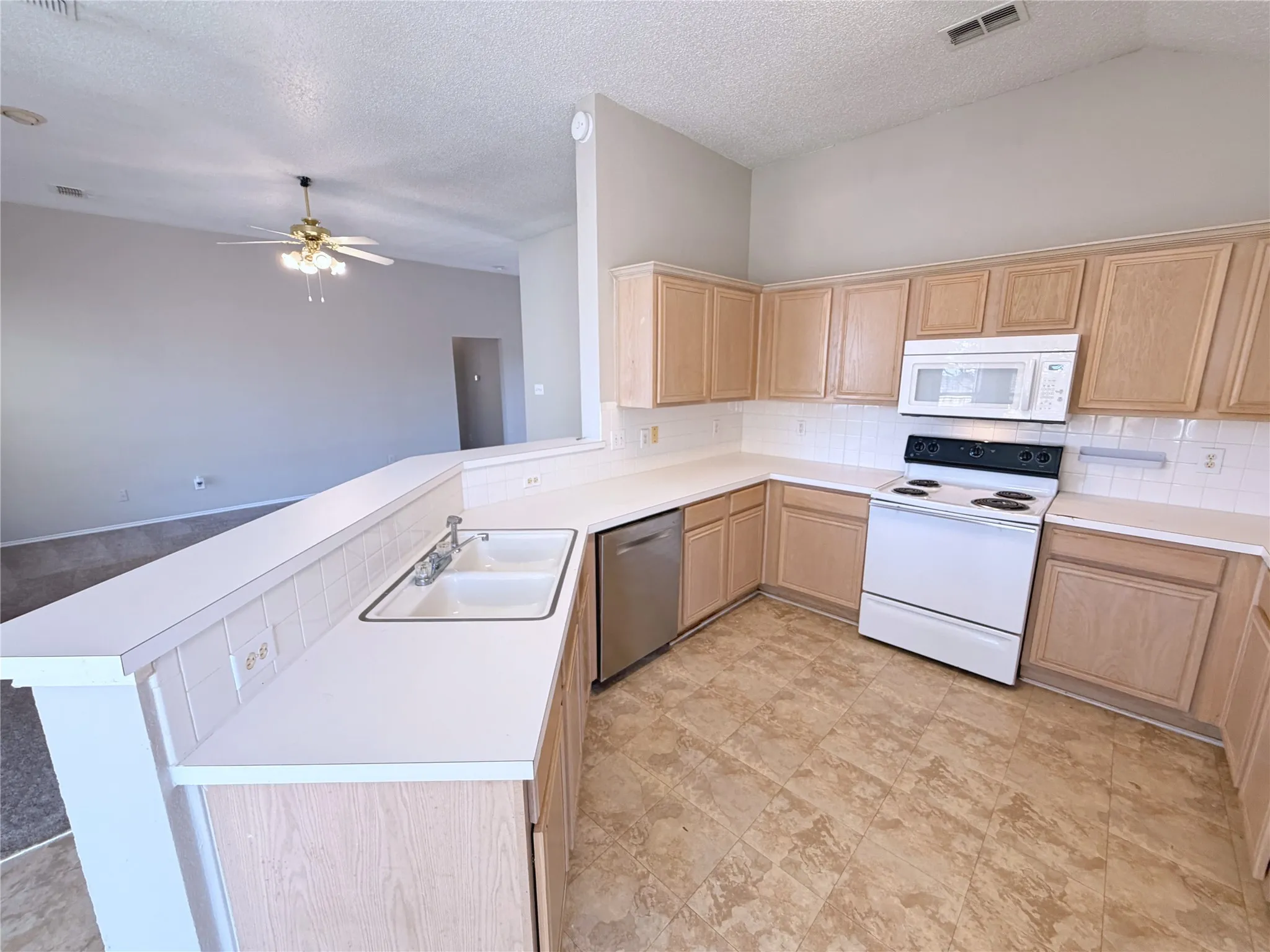 Kitchen with light wood-finish cabinetry, white countertops, a tile backsplash, and a double basin sink