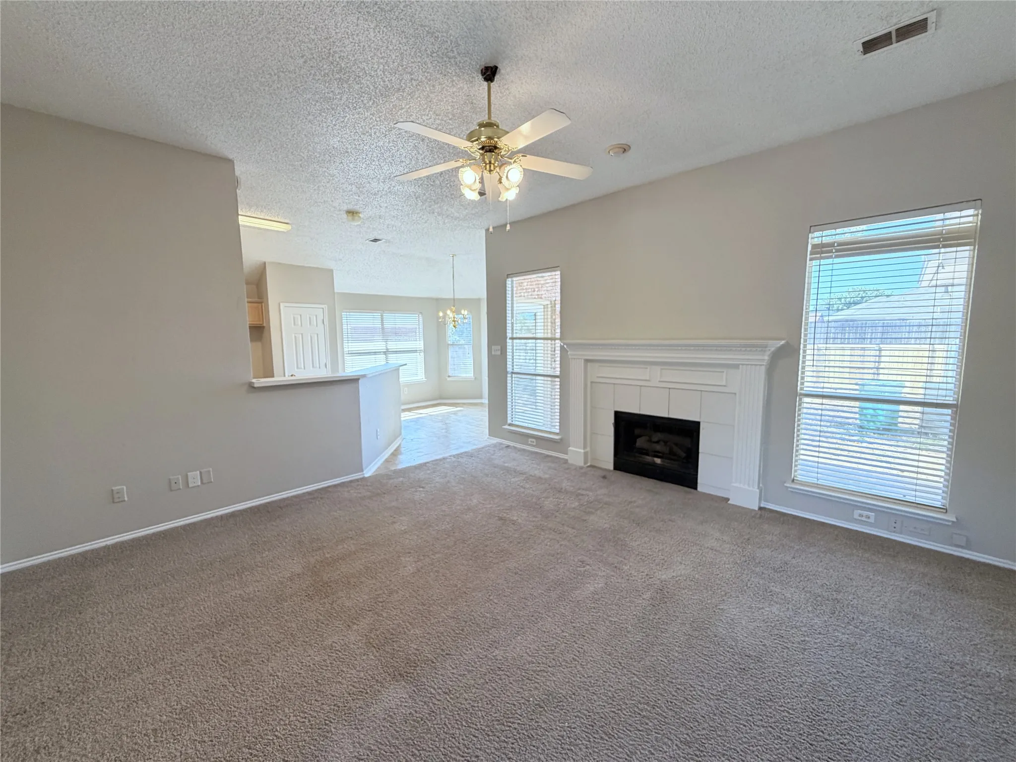 Carpeted living area featuring a central ceiling fan, white trim work, and a fireplace with a white mantel and tile surround