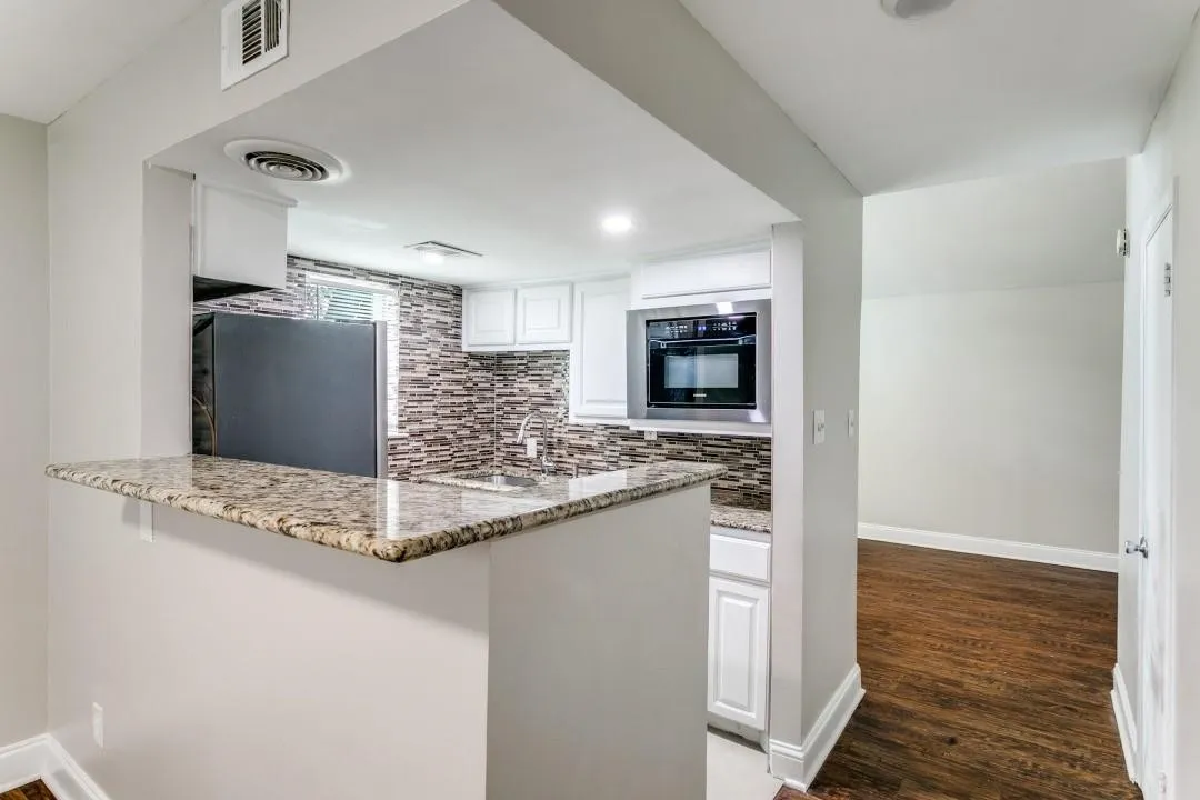 Kitchen featuring a breakfast bar with stone countertop, white cabinetry, integrated microwave, and mosaic tile backsplash