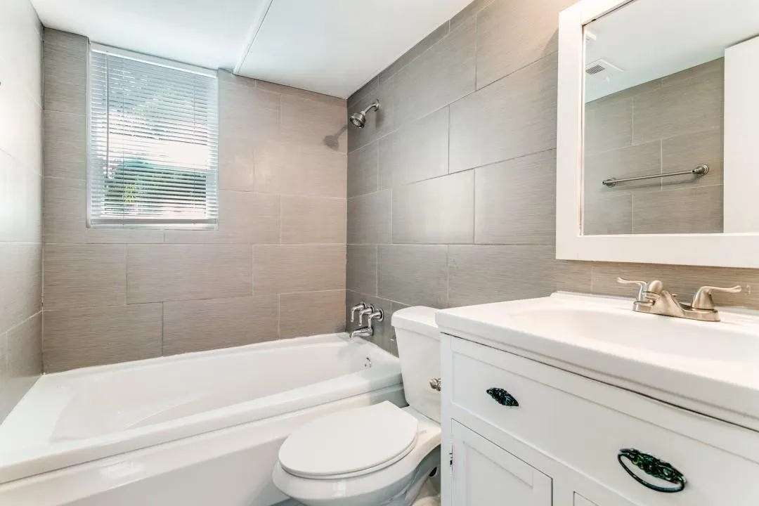 Bathroom featuring a white vanity with integrated sink, brushed nickel faucet, wall-mounted mirror, and tile-surround bathtub with shower head
