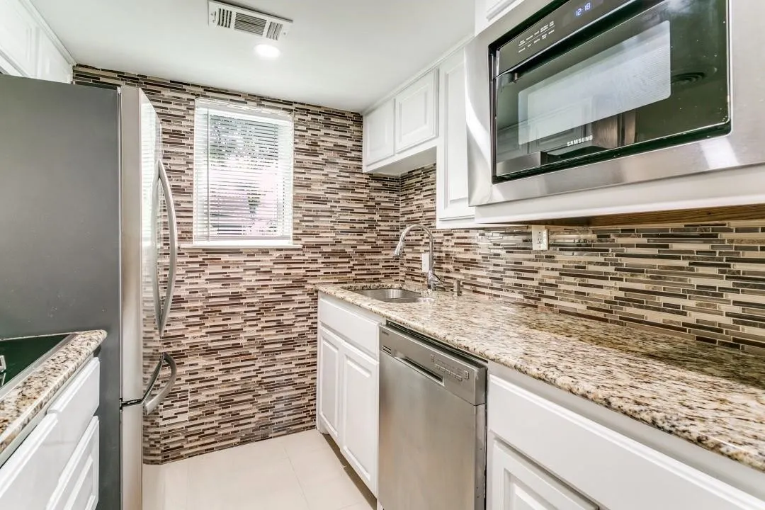 Kitchen featuring white cabinetry, stainless steel appliances, granite countertops, and a full tile backsplash