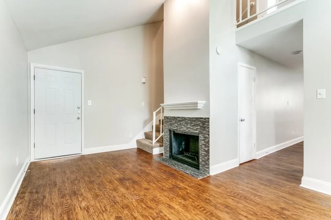 Vaulted ceiling, wood-finish flooring, tiled fireplace surround with mantel, interior staircase with railing, and white interior doors