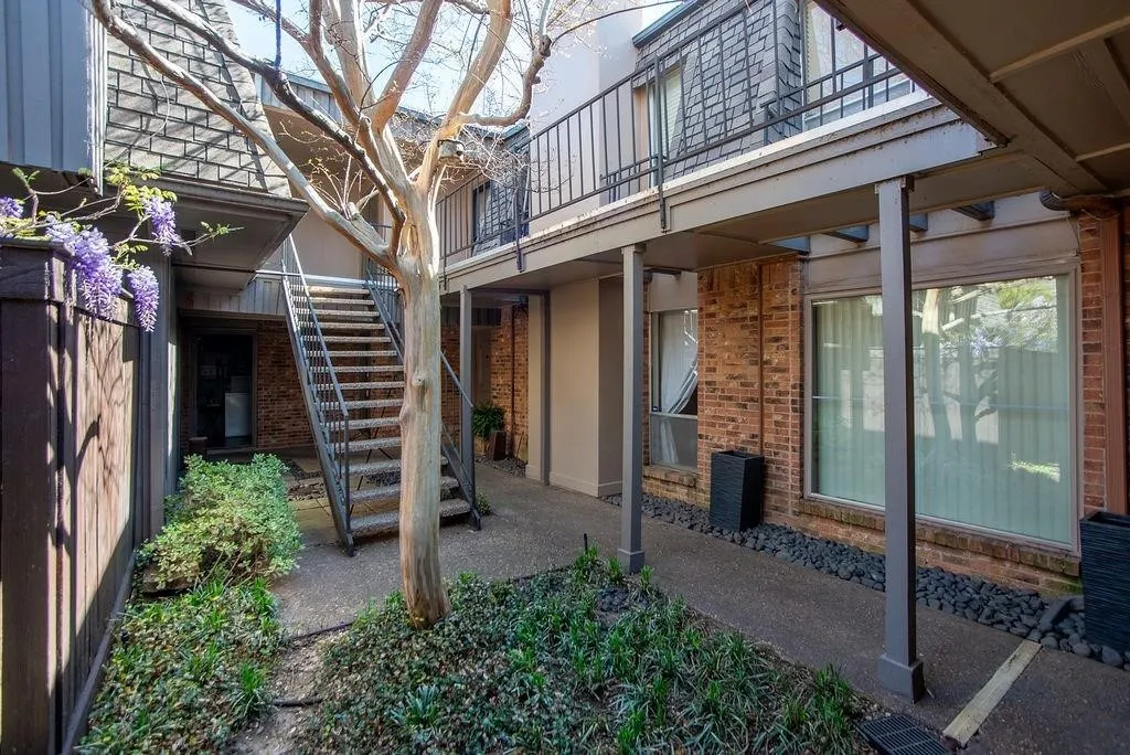 Courtyard entry featuring a mature tree, metal staircase, brick exterior, and covered walkway
