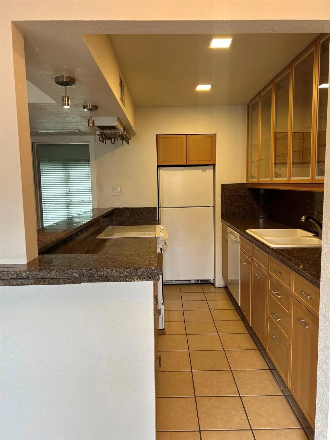 Kitchen featuring tile flooring, wood cabinetry with glass-front uppers, solid surface countertops, and recessed lighting