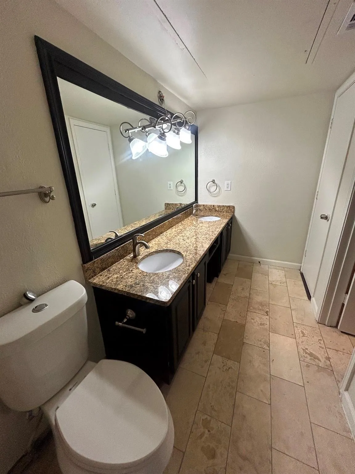 Dual vanity with granite-style countertop, undermount sinks, dark wood-finish cabinetry, and tiled flooring