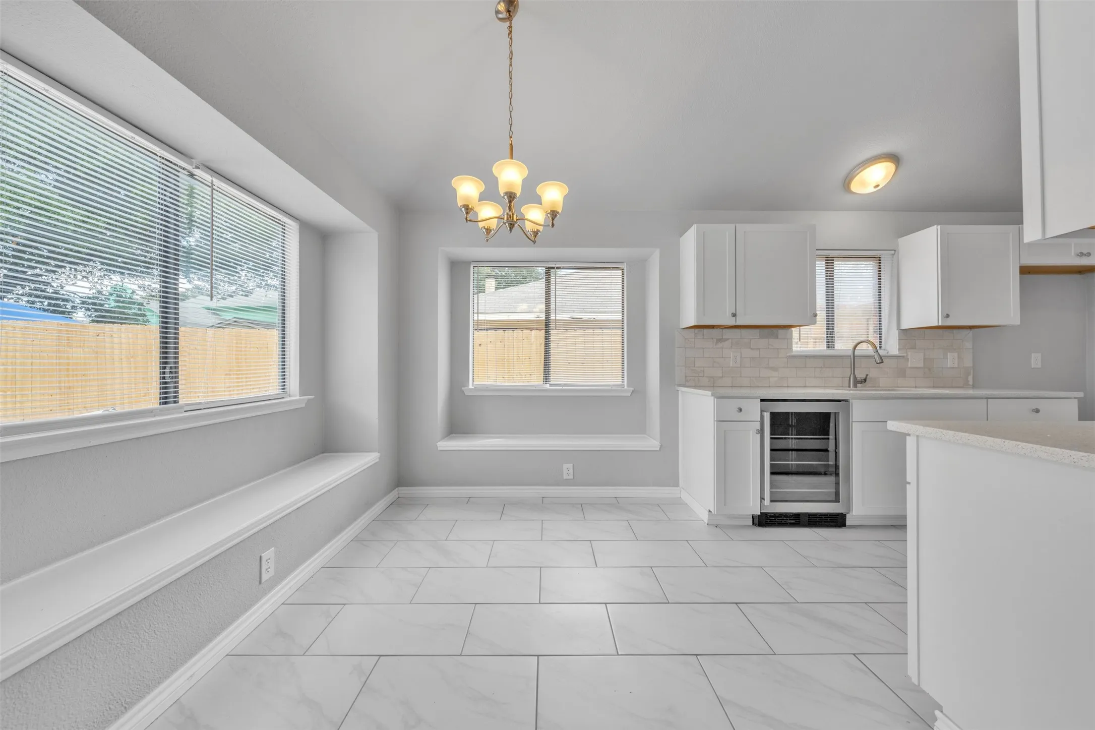 Open concept kitchen with white cabinetry, stainless steel beverage refrigerator, and subway tile backsplash