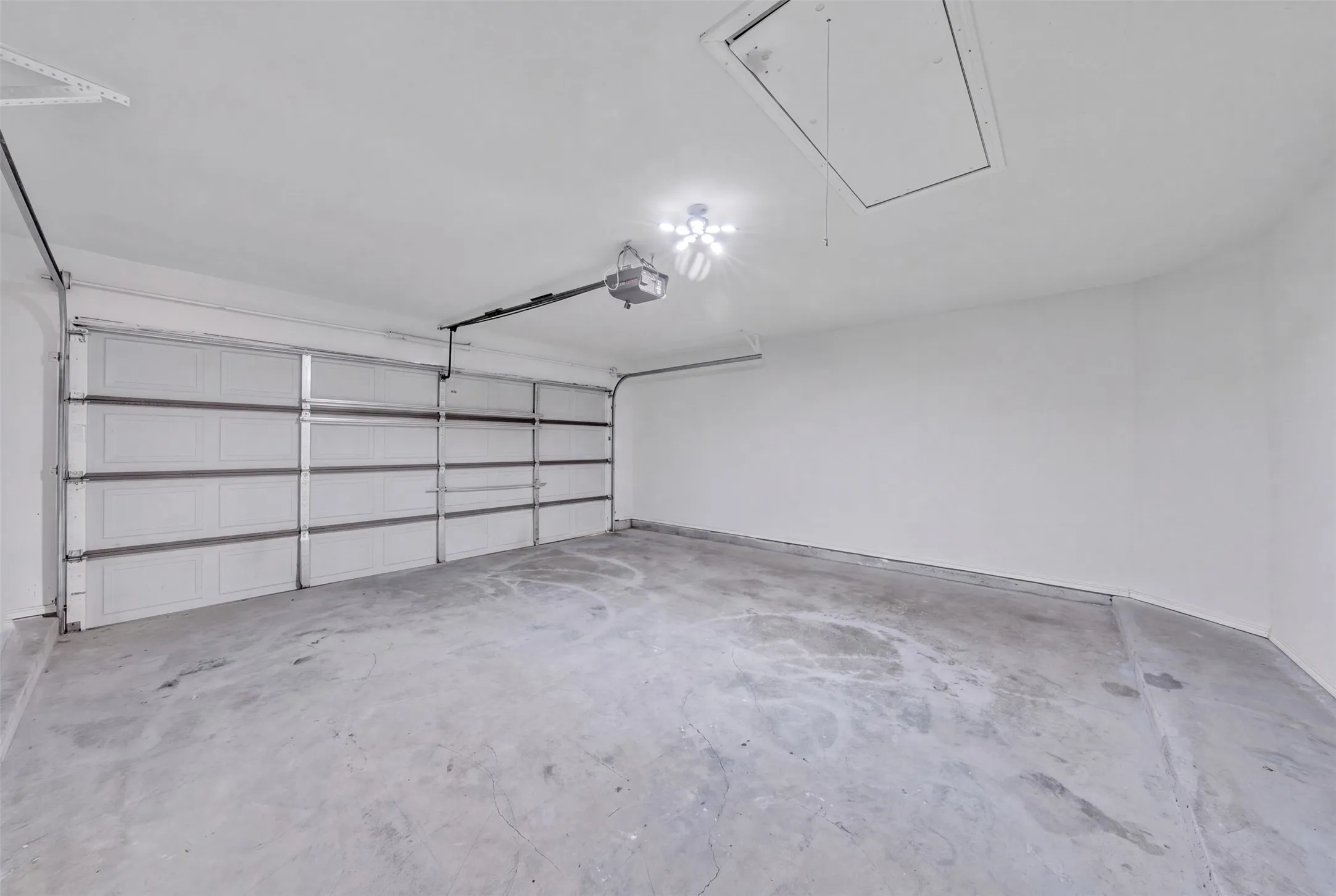 Attached garage featuring multiple overhead doors, concrete flooring, overhead lighting, and an attic access panel