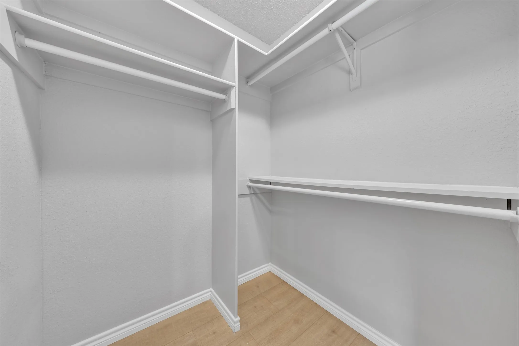 Walk-in closet featuring white built-in shelving, white hanging rods, and wood-finish flooring