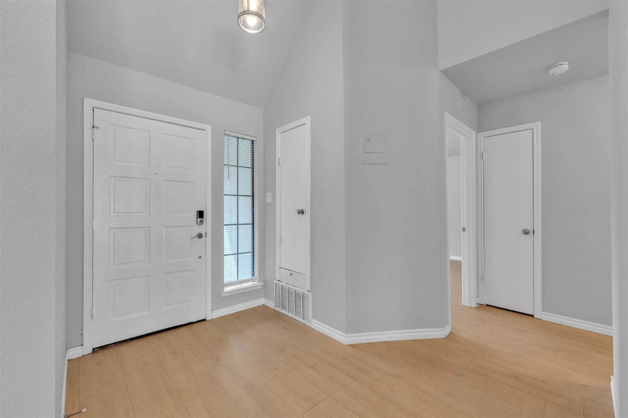 Vaulted ceiling entry with wood-finish flooring, white panel door, and side light window