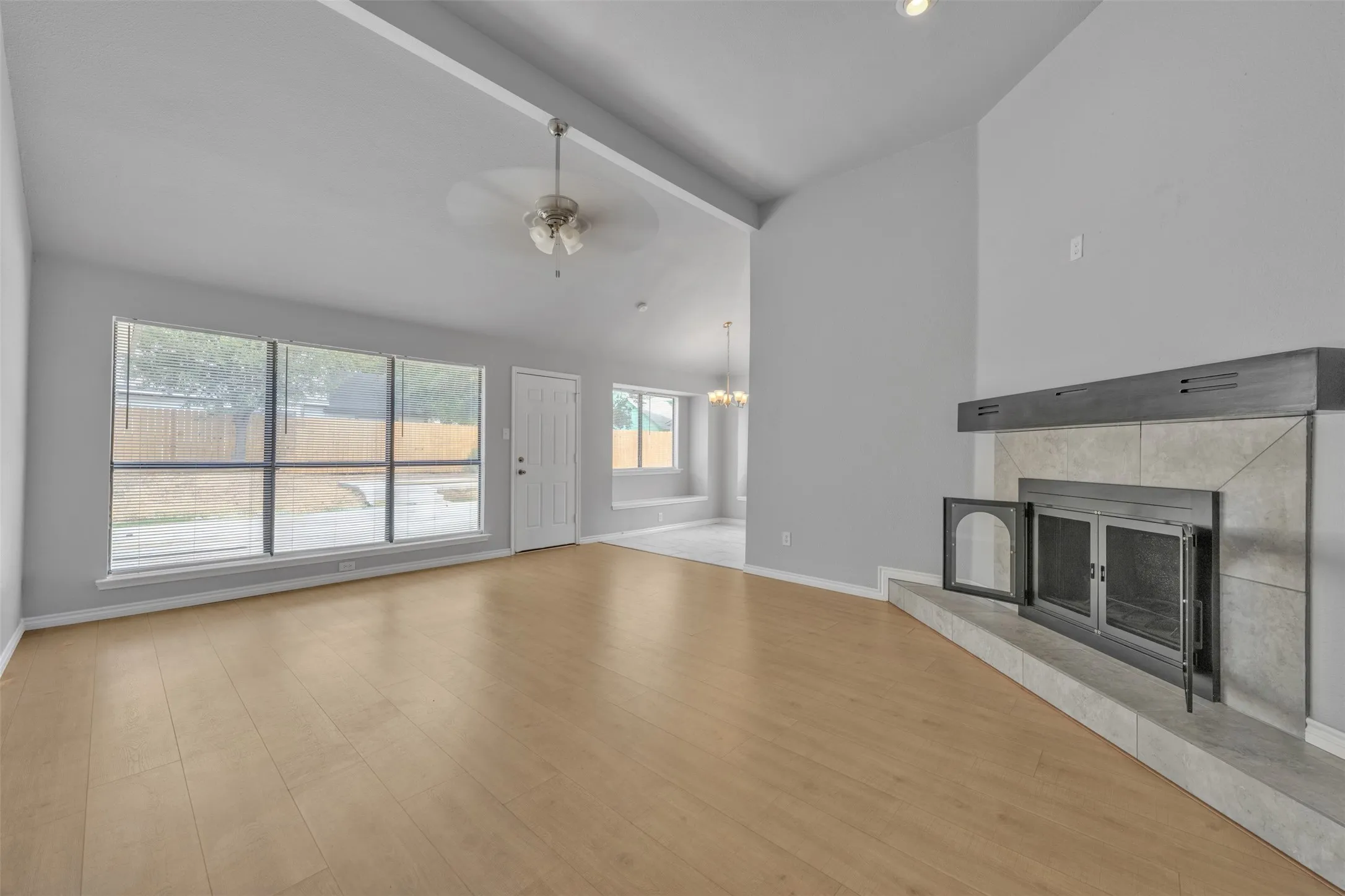 Vaulted ceiling with a ceiling fan, wood-finish flooring, a fireplace with a tile surround and hearth, and large windows