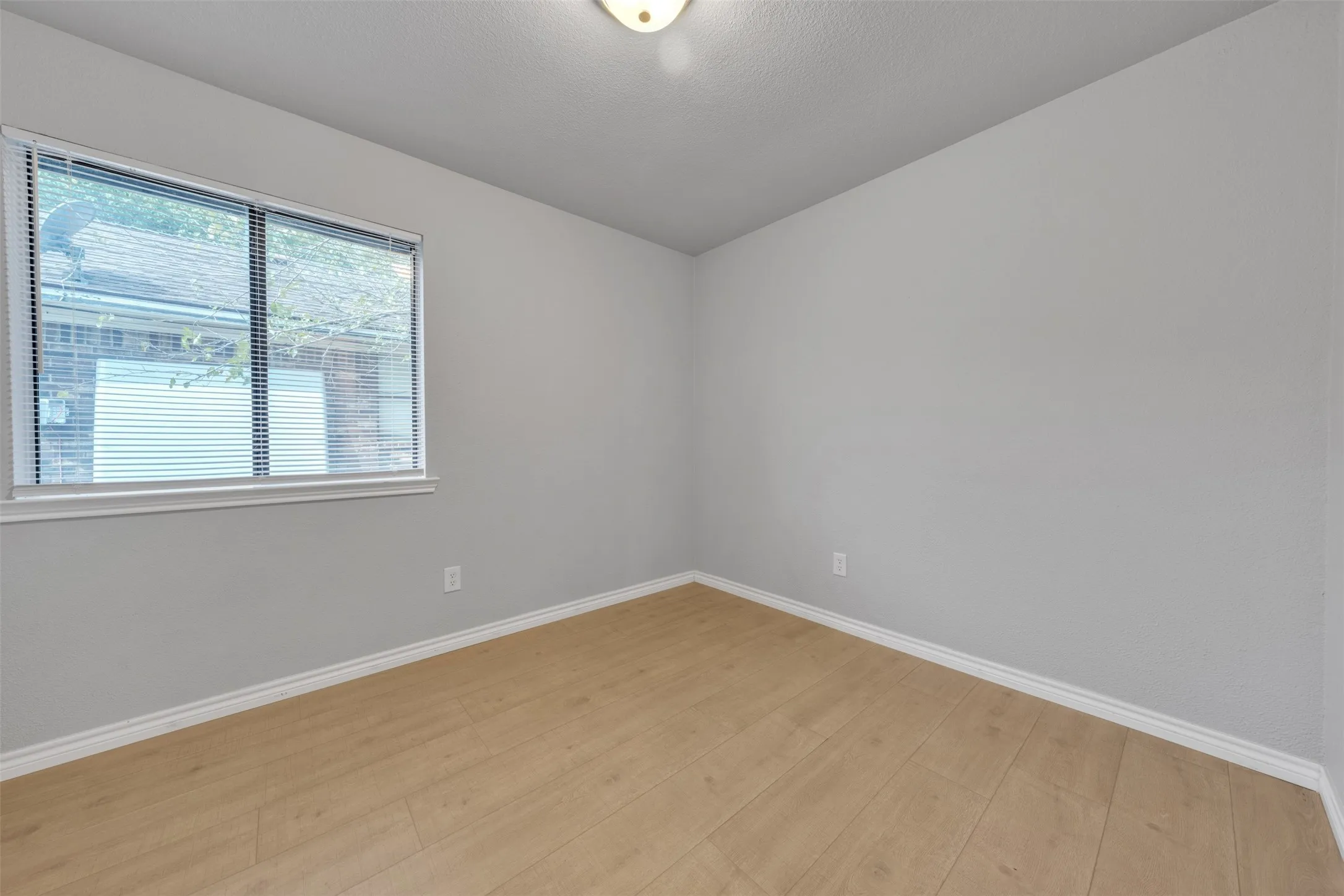 Wood-finish flooring with white trim, light gray walls, and a window with blinds