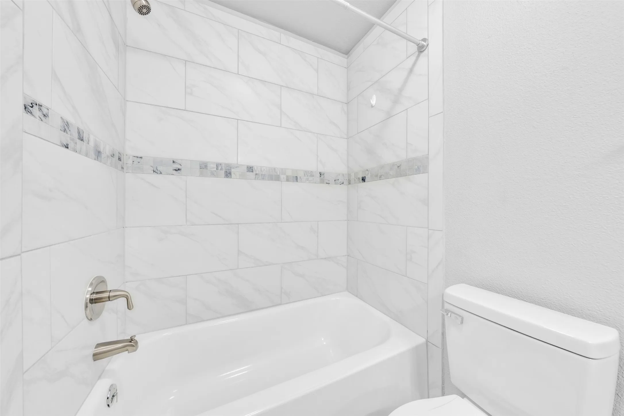 White subway-style tile shower surround with a decorative mosaic accent band