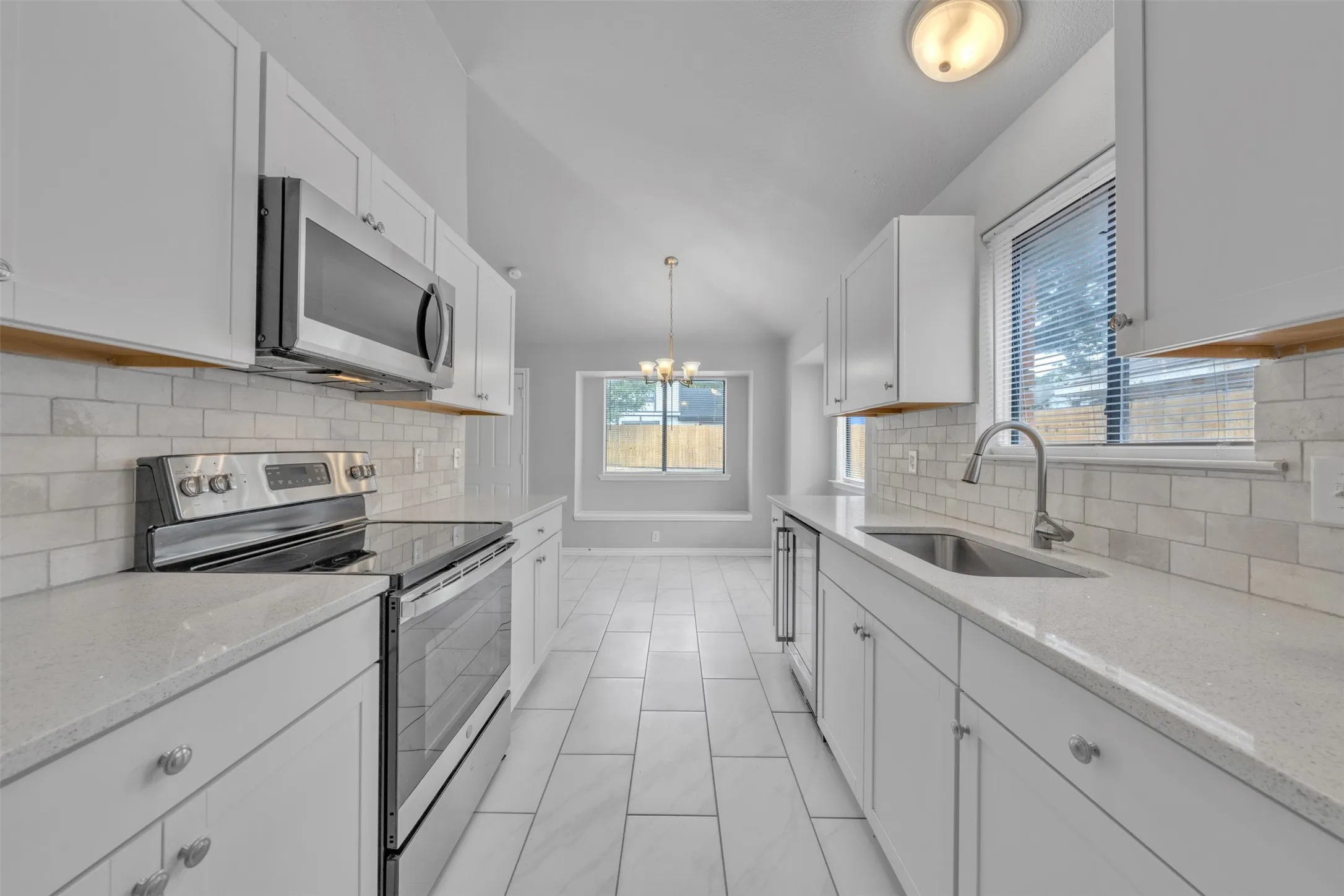 Vaulted ceiling kitchen featuring white cabinetry, light-toned countertops, subway tile backsplash, and stainless steel appliances