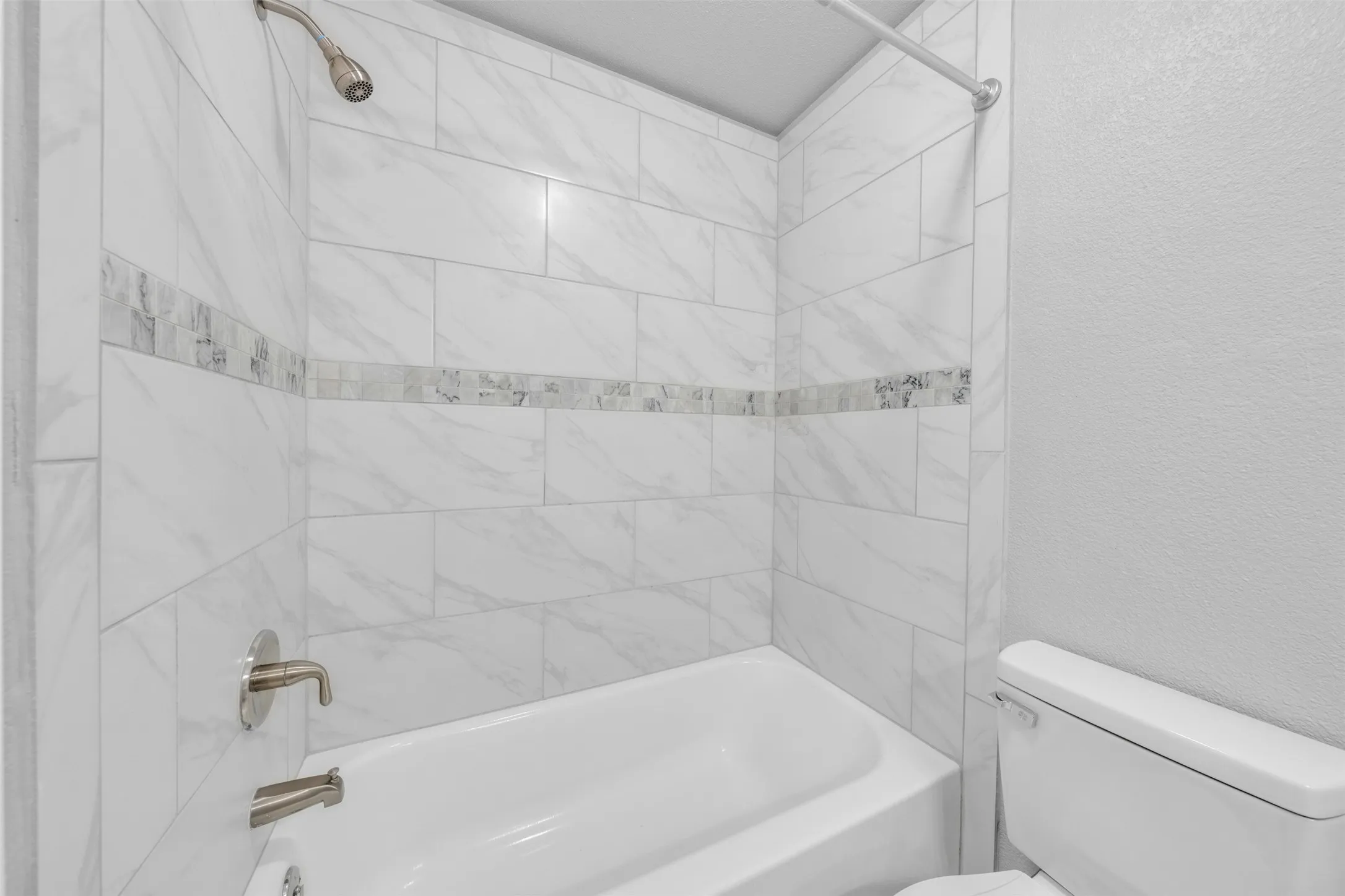 Bathtub with subway tile surround, decorative mosaic tile accent, and brushed nickel fixtures