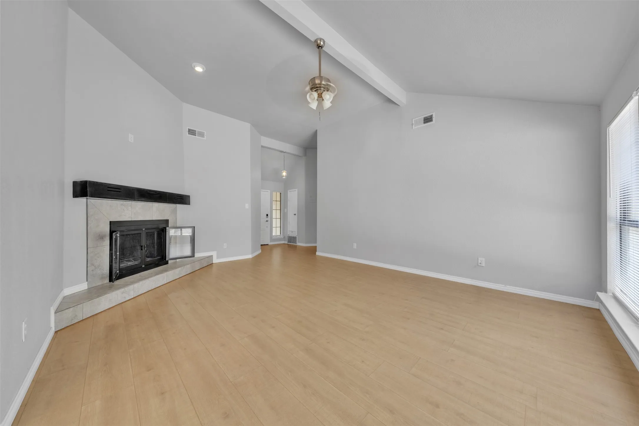 Spacious room featuring vaulted ceilings with exposed beams, recessed lighting, wood-finish flooring, and a fireplace with a stone surround