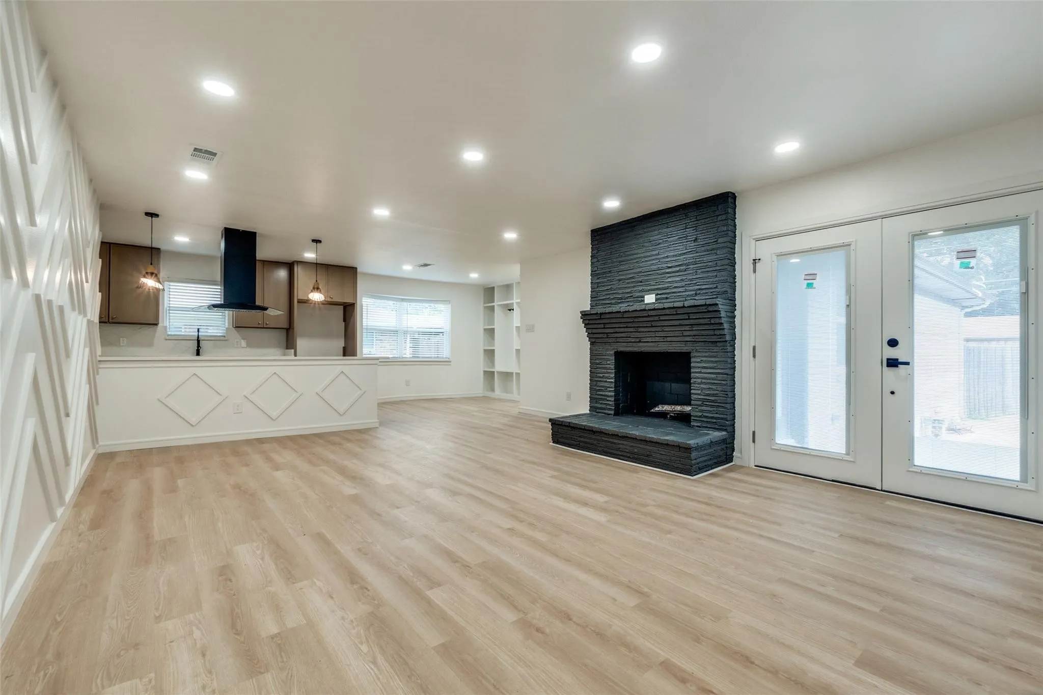Wood-finish flooring, recessed lighting, accent wall, brick-clad fireplace, and double French doors