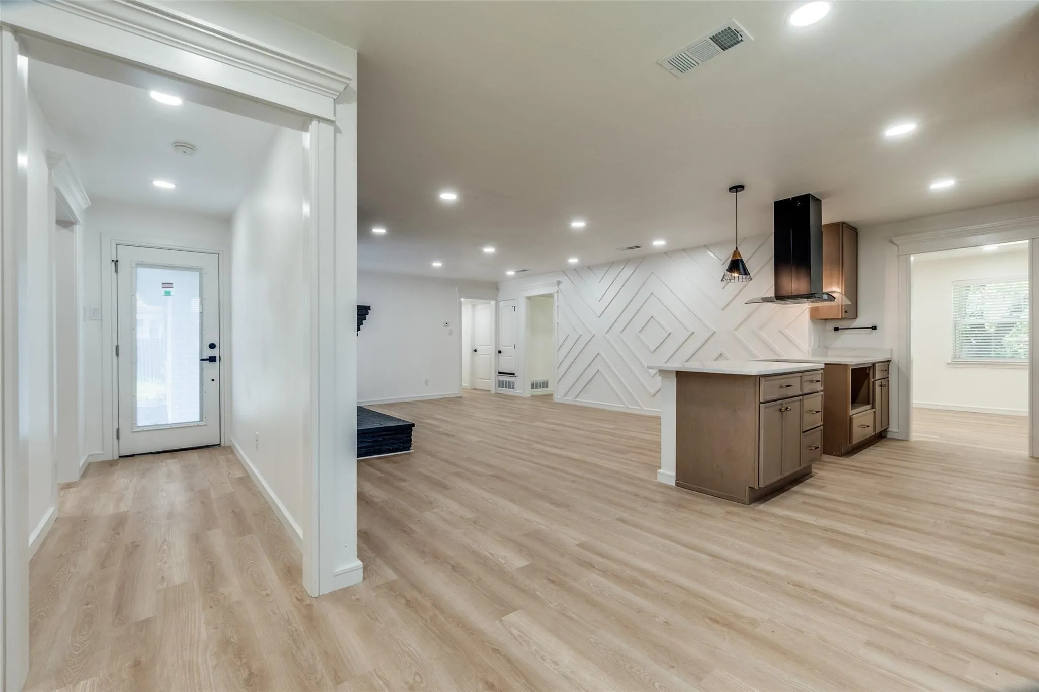 Open-concept living space featuring light wood-finish flooring throughout, recessed ceiling lighting, and a central kitchen island with wood cabinetry