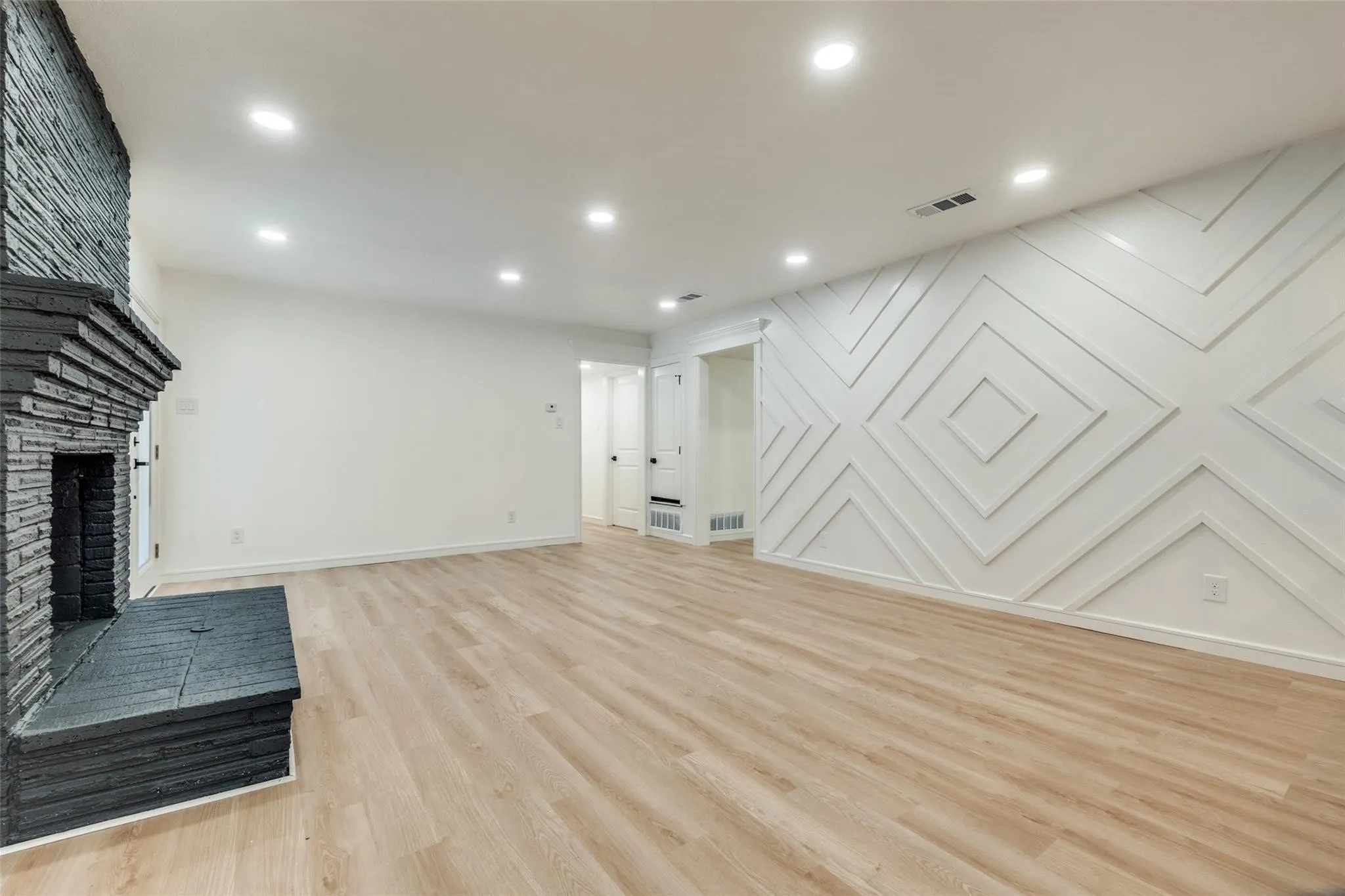 Recessed lighting, light wood-finish flooring, a stacked stone fireplace with hearth, and a geometric accent wall