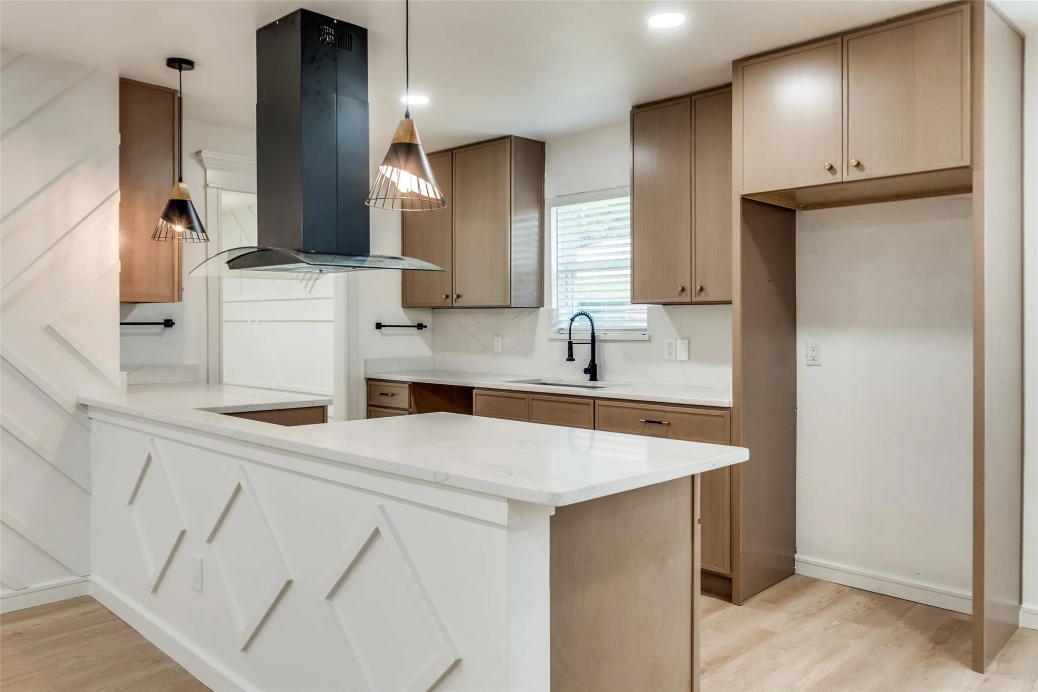 Kitchen featuring wood-finish cabinetry, white countertops, a black range hood, and a built-in refrigerator enclosure