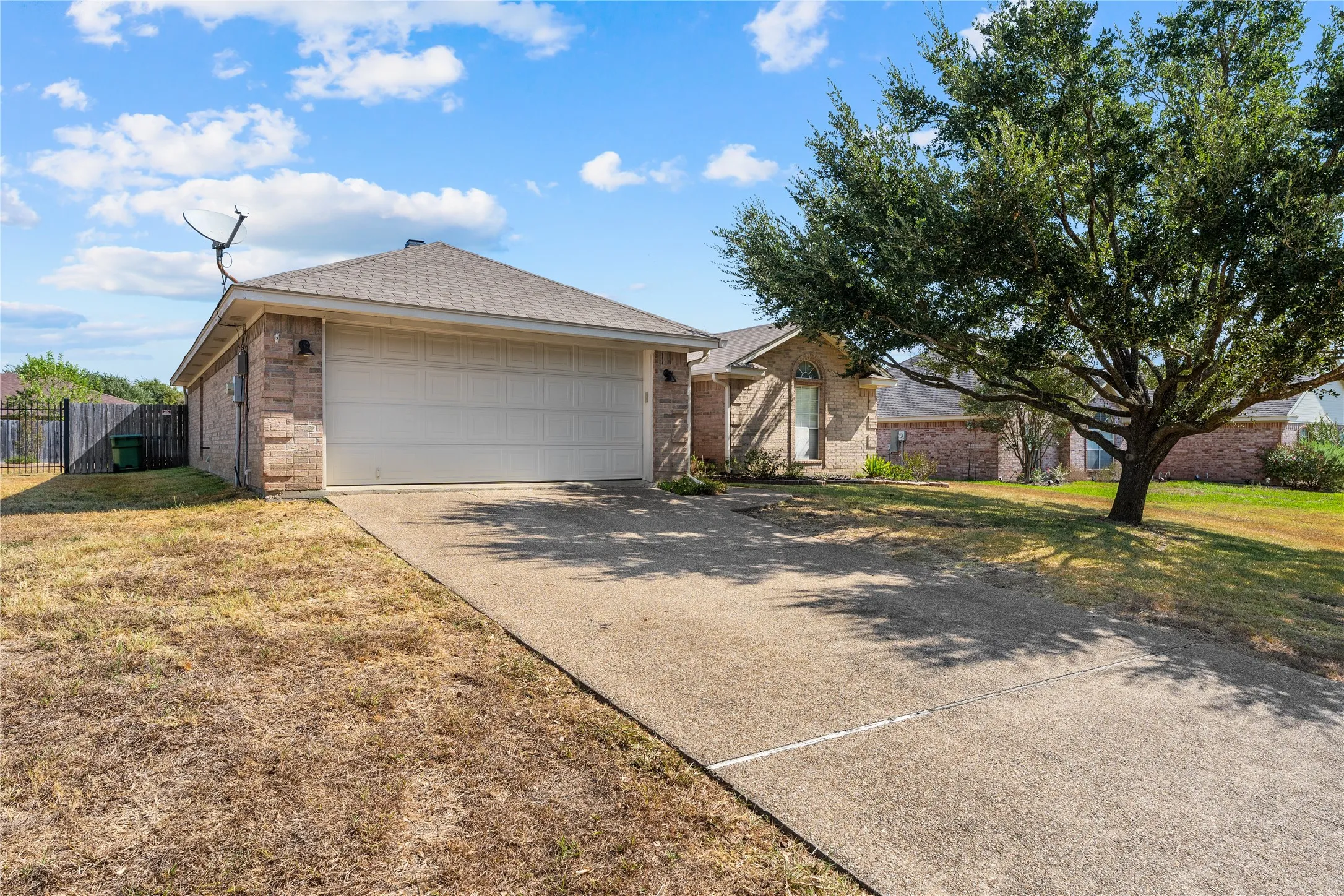 Brick exterior with an attached garage, paved driveway, and mature trees