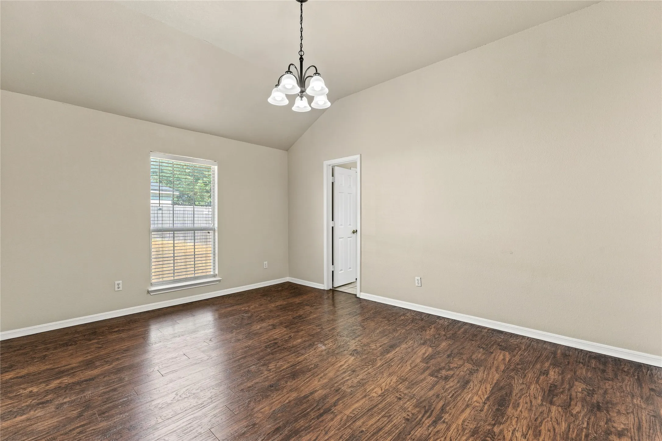 Vaulted ceiling, wood-finish flooring, window with blinds, chandelier, painted walls