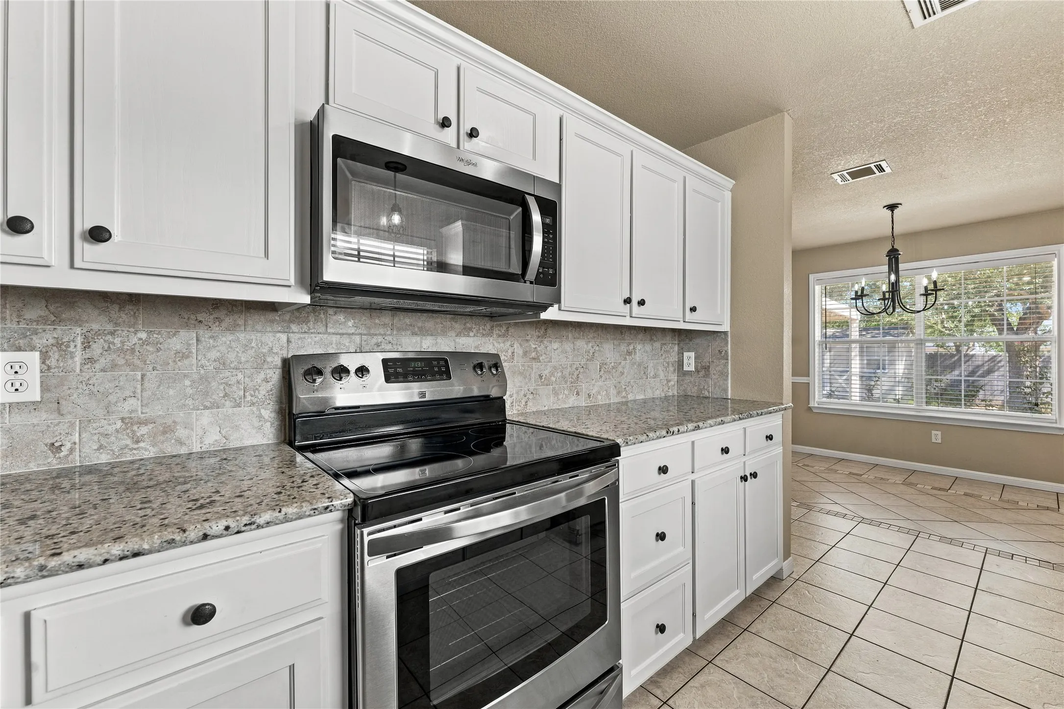 White cabinetry with dark hardware, stainless steel appliances, speckled countertops, tile backsplash, and tile flooring