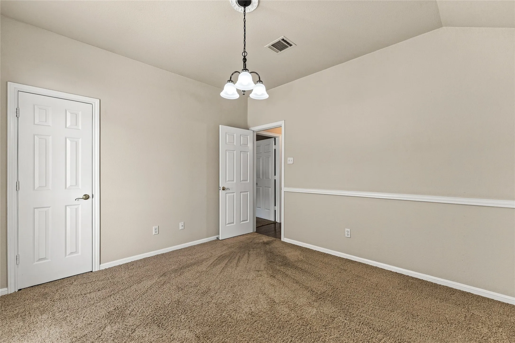 Carpeted room with vaulted ceiling and a three-light chandelier