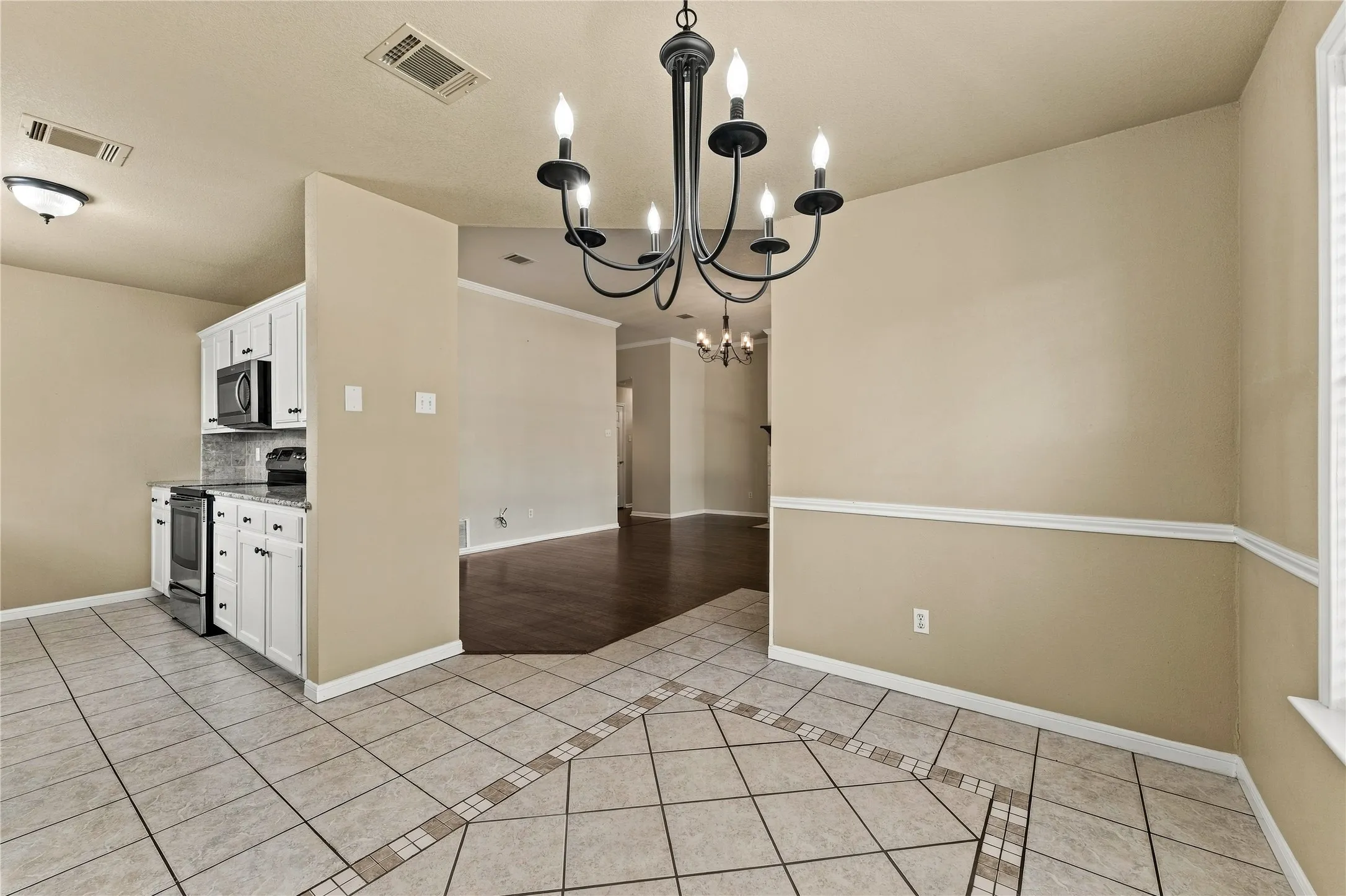 Tile flooring with an inlaid pattern, a chandelier, white cabinetry, a stainless steel oven/range, and a built-in microwave