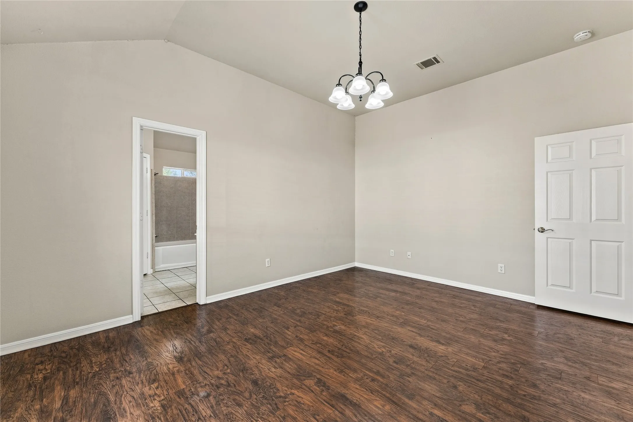 Vaulted ceiling with an attached chandelier, wood-finish flooring, and a six-panel interior door