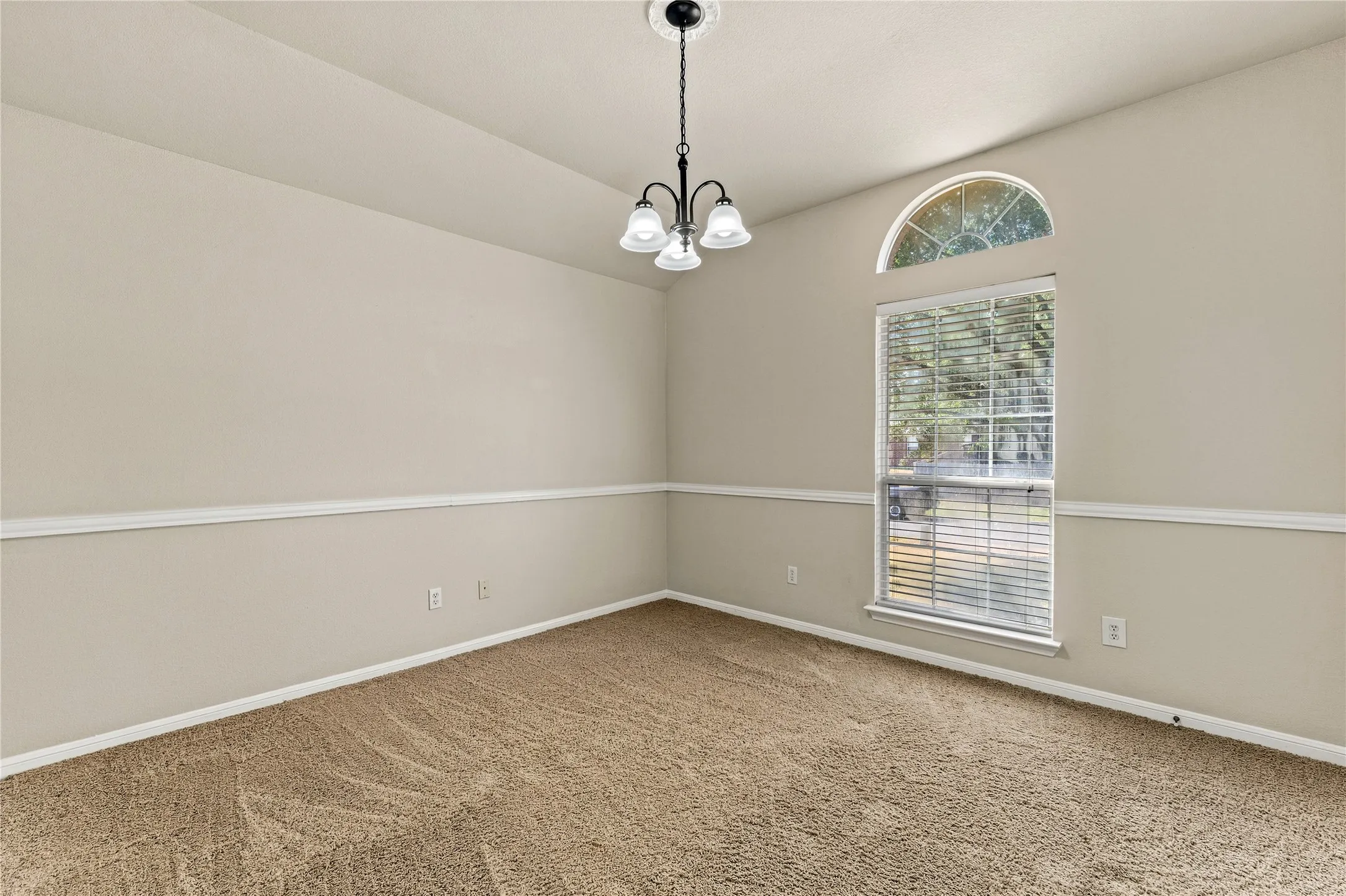 Room featuring textured carpeting, a window with an arched transom, and a contemporary pendant light fixture