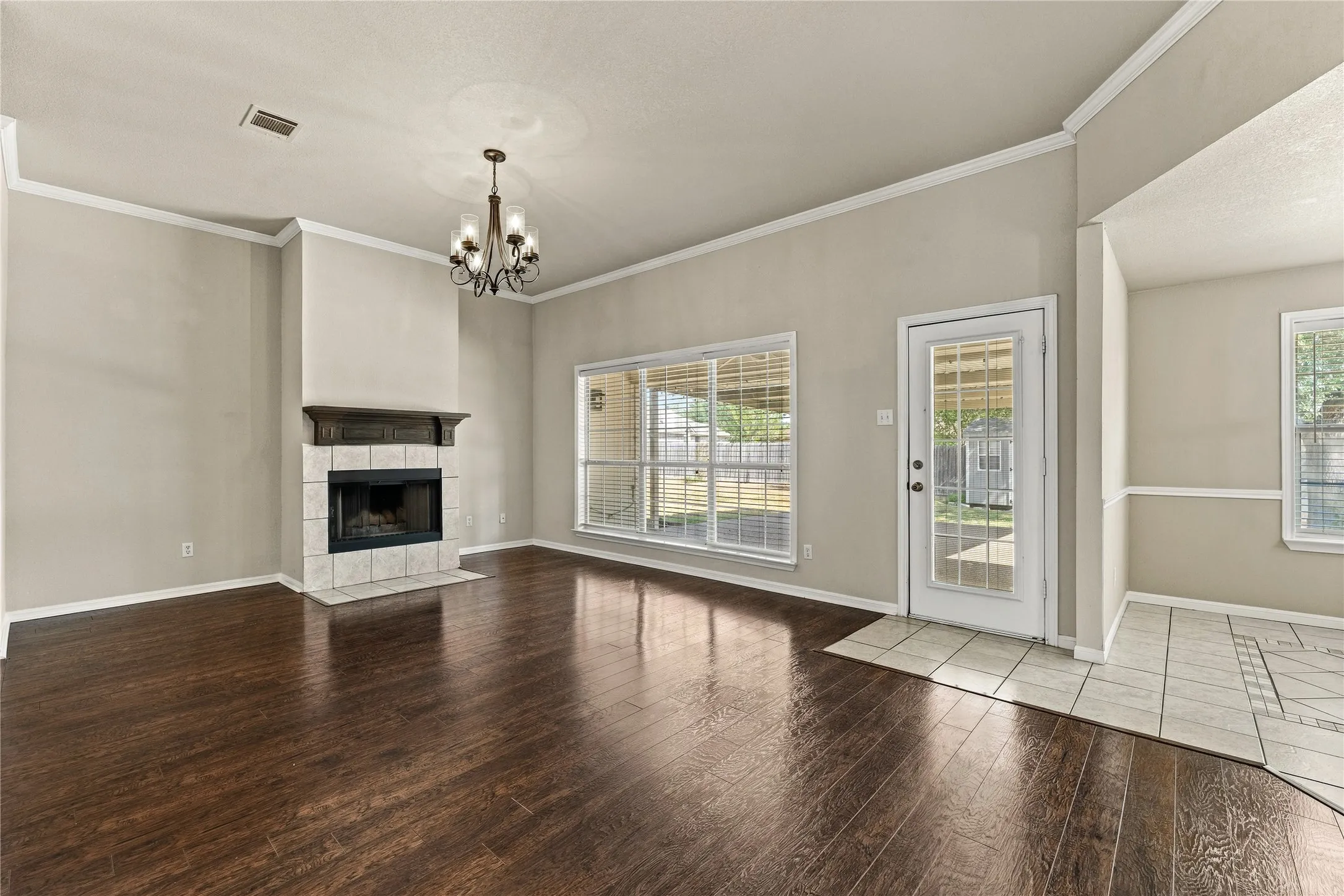 Wood-finish flooring, tiled fireplace with mantel, ceiling-mounted chandelier, glass-paneled exterior door, and multiple windows
