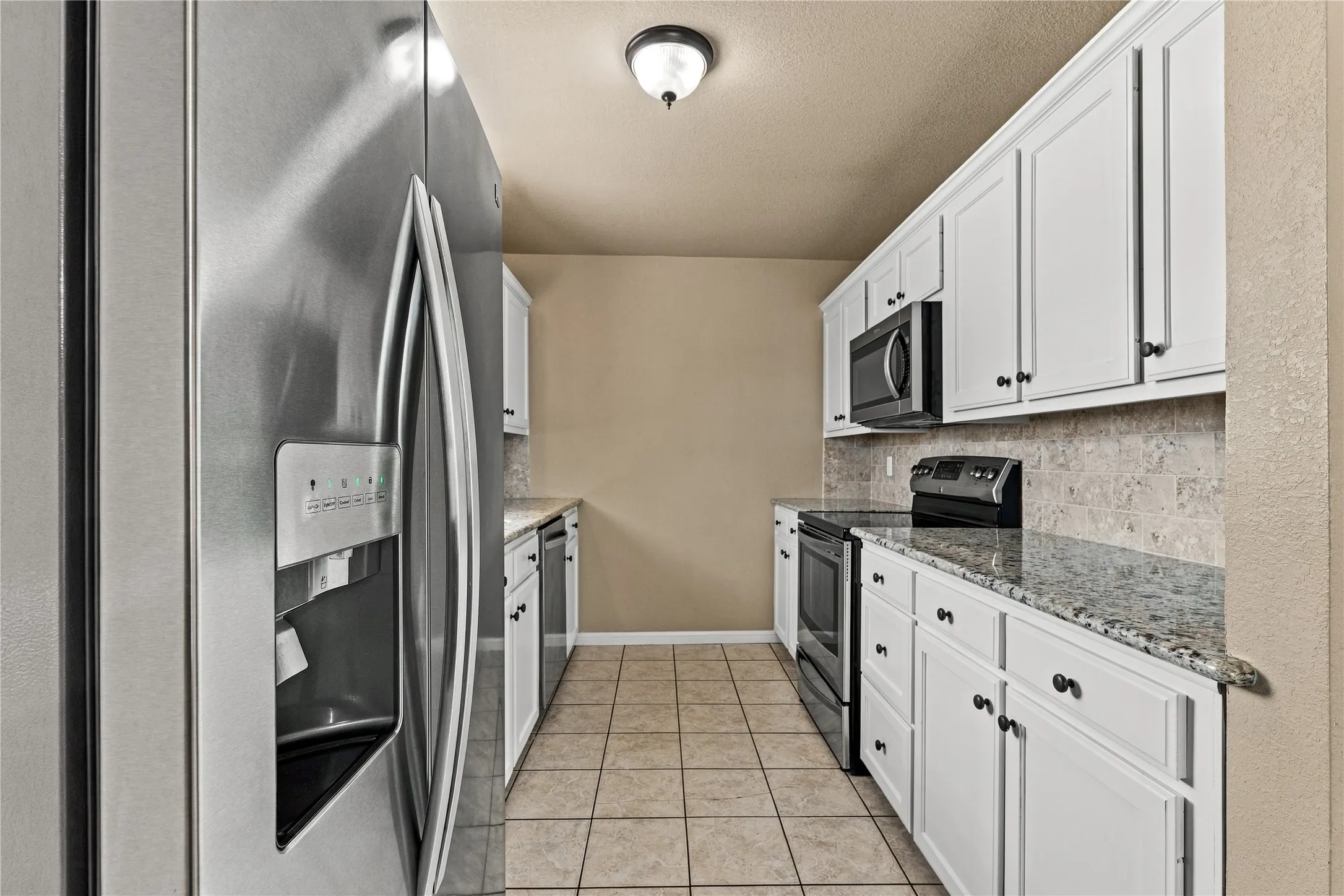 Galley kitchen featuring white cabinetry, granite countertops, tile backsplash, stainless steel appliances, and tile flooring