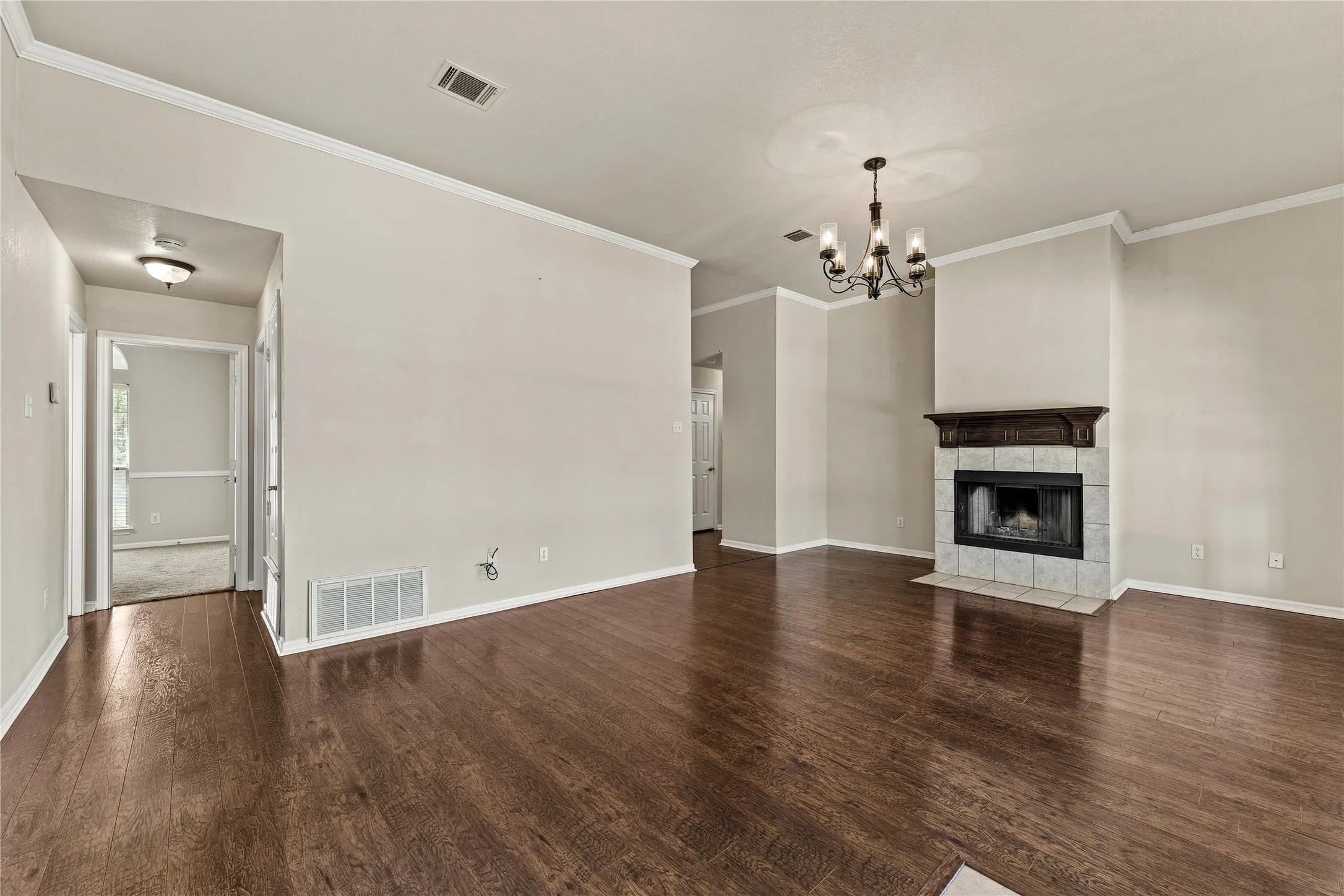 Hardwood-finish flooring, recessed fireplace with tile surround, decorative mantel, chandelier lighting, and crown molding