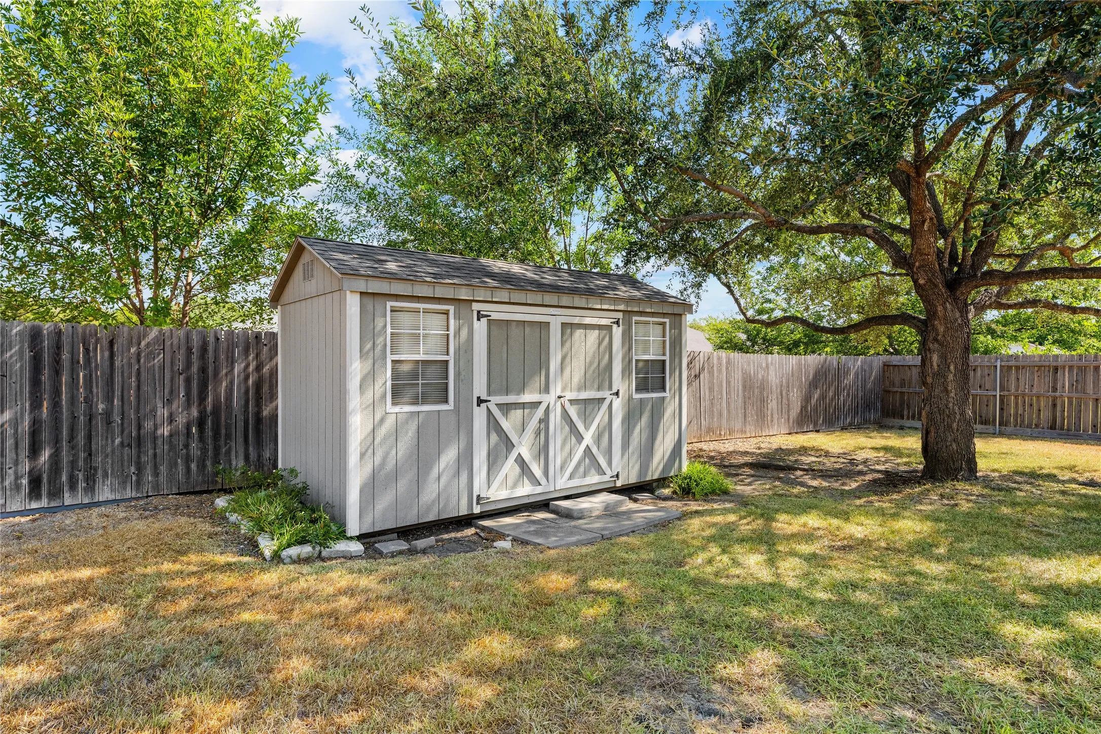 Detached storage shed with double barn doors and two windows, set on a stone paver foundation